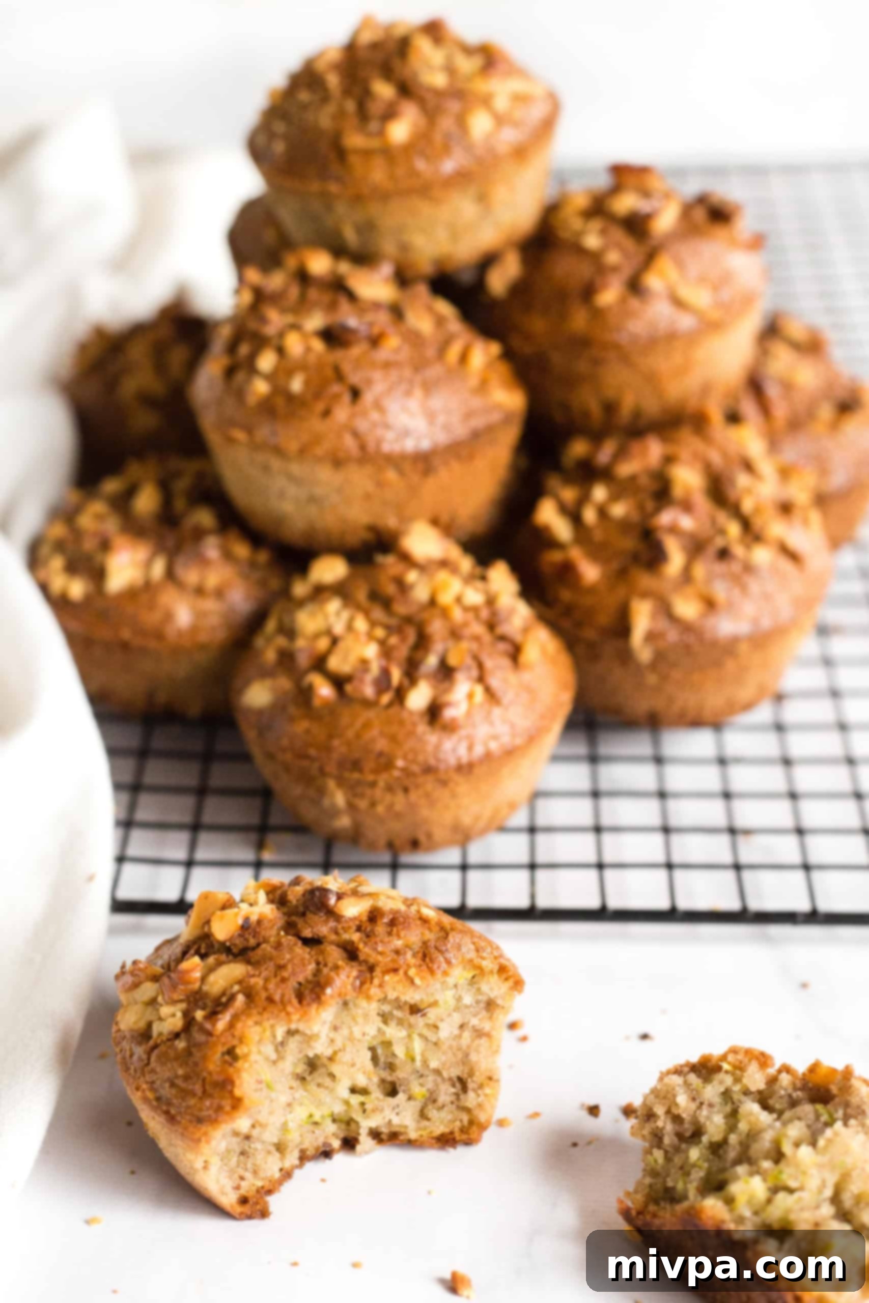 Half-eaten zucchini muffin in front of a stack on muffins on a cooling rack.