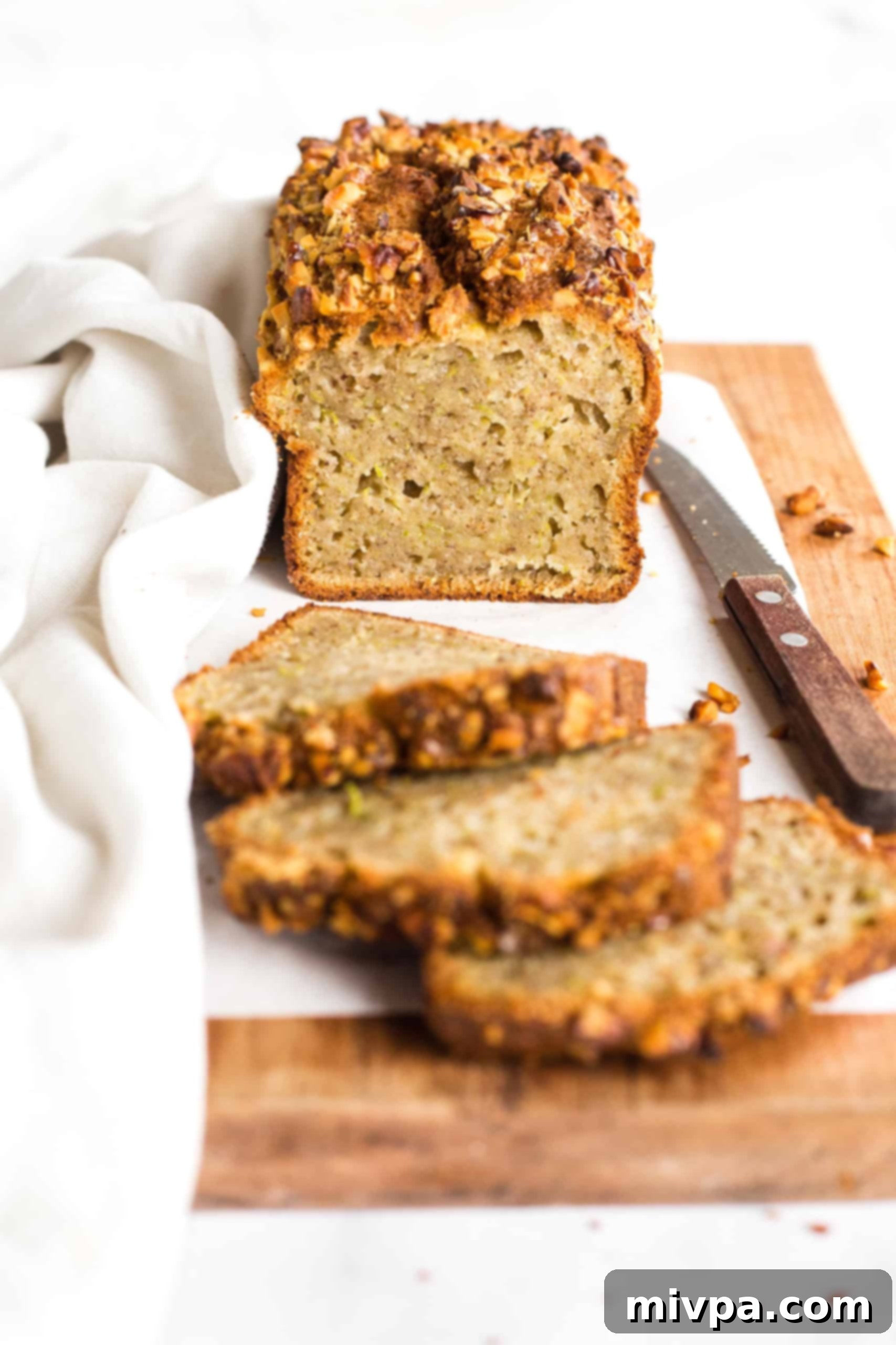 Half-sliced loaf of gluten-free dairy-free zucchini bread on a parchment-lined wooden board, showcasing its moist interior and golden crust.
