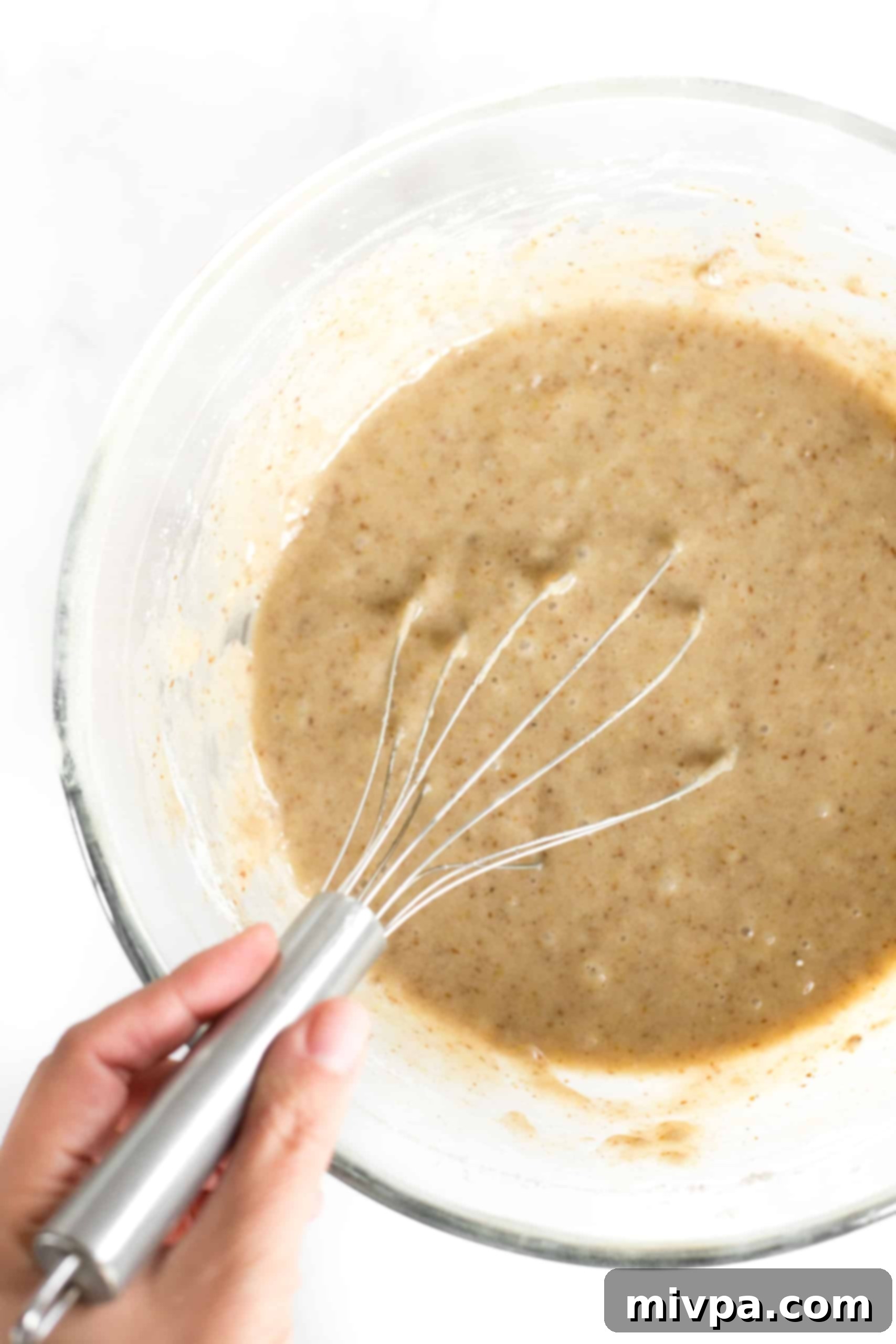 A spatula gently mixing the zucchini bread batter in a large glass bowl, showing the transition from dry to wet ingredients.