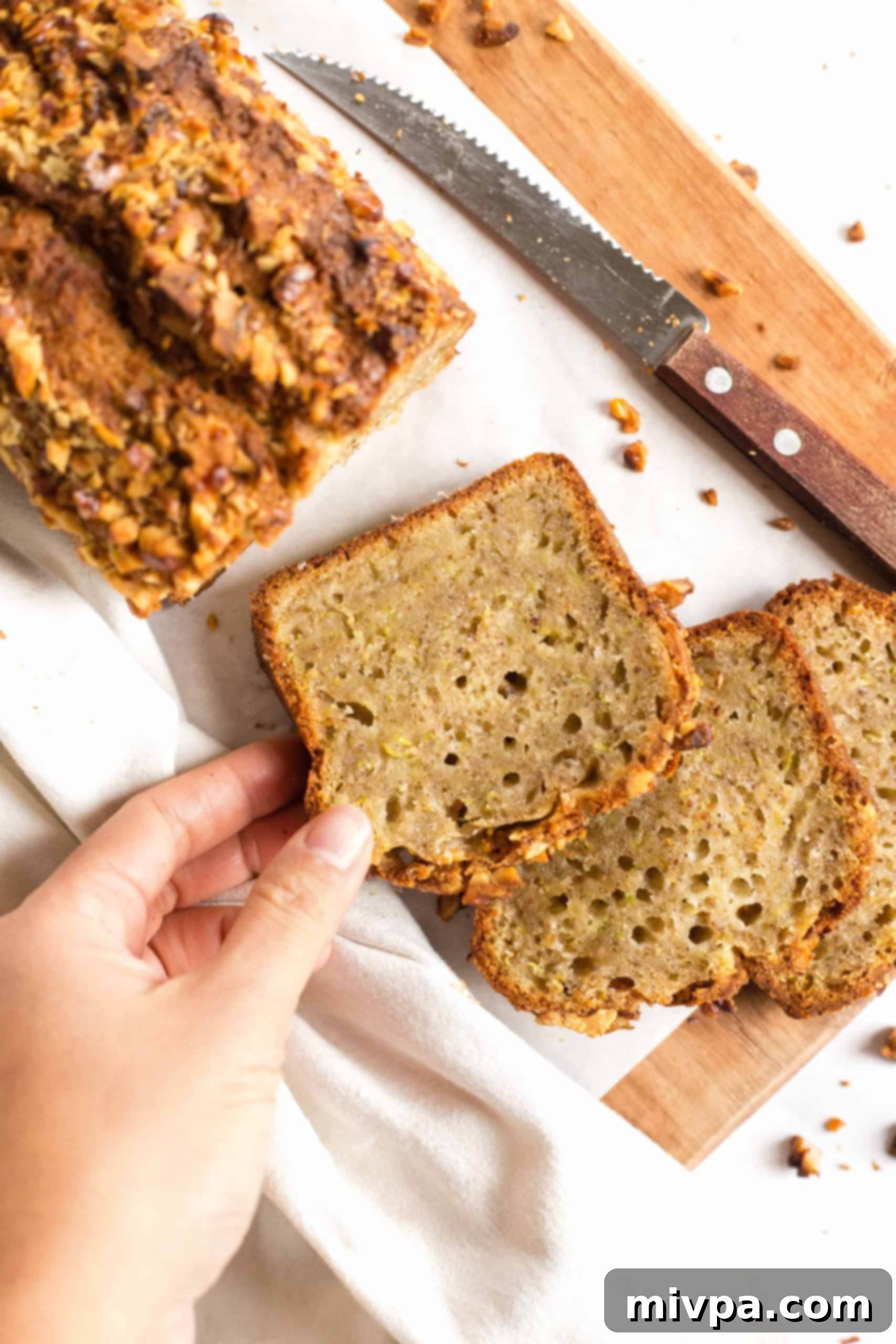 Reaching for a fresh, golden slice of gluten-free zucchini bread from a wooden board, ready to be enjoyed.