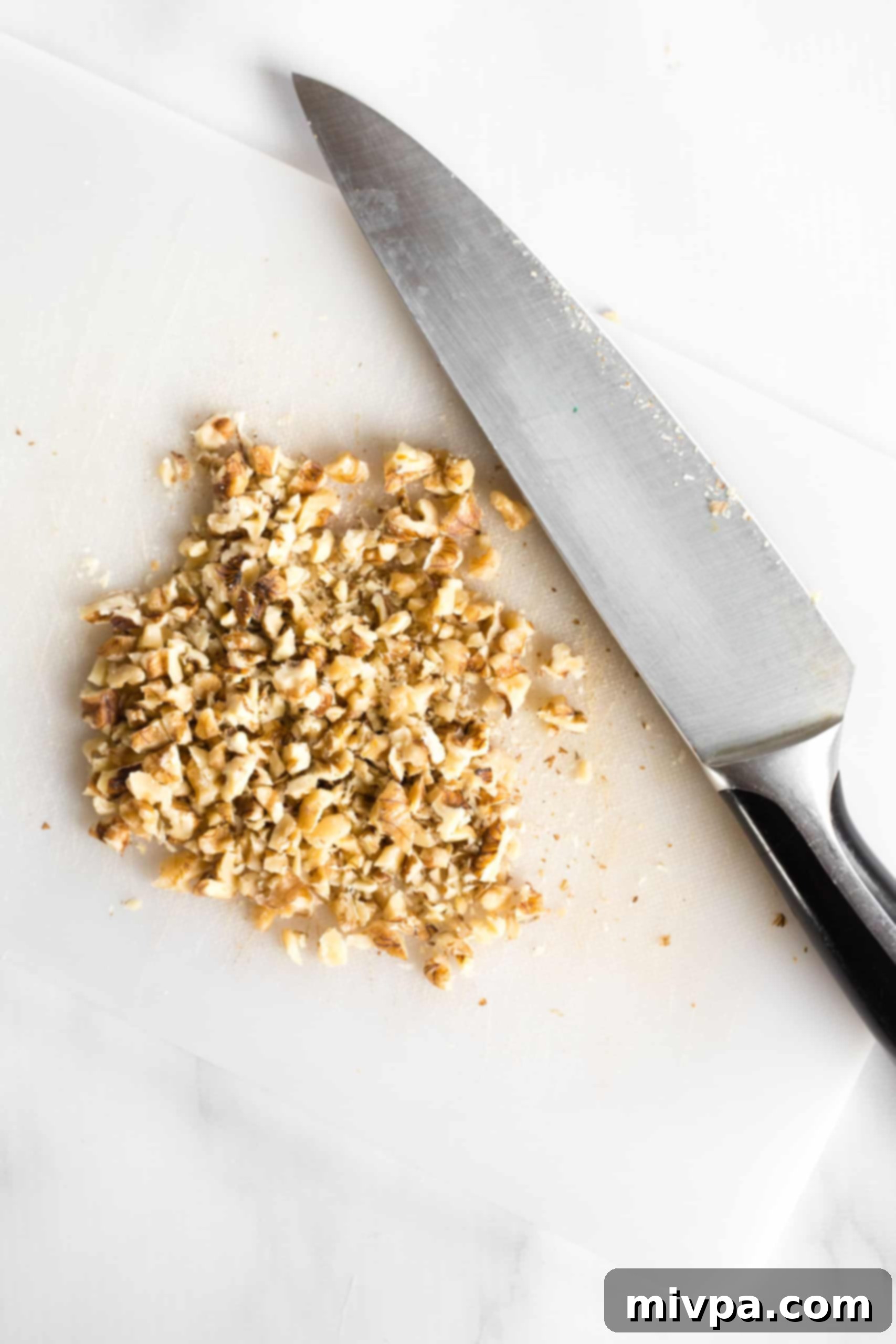 Roughly chopped walnuts arranged on a chopping board alongside a large chef's knife.