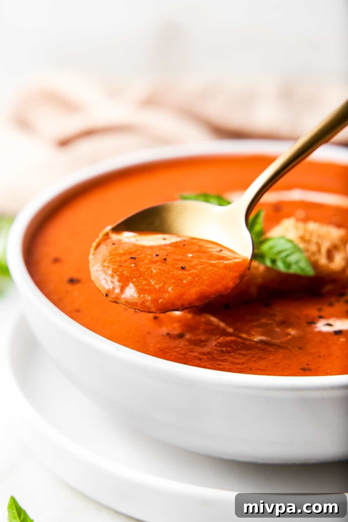 A spoon scooping up tomato soup from a bowl.
