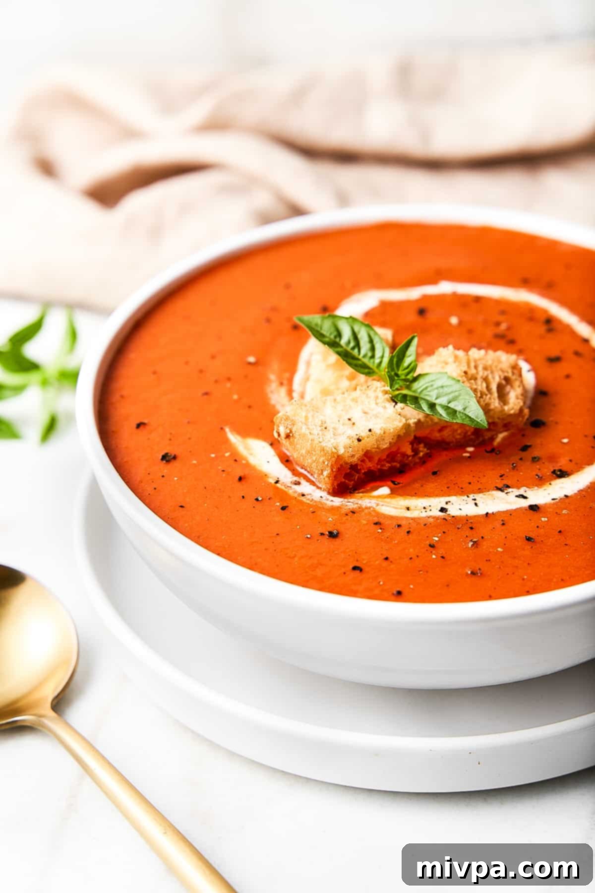 A bowl of gluten-free tomato soup with sour cream, croutons, basil and pepper.