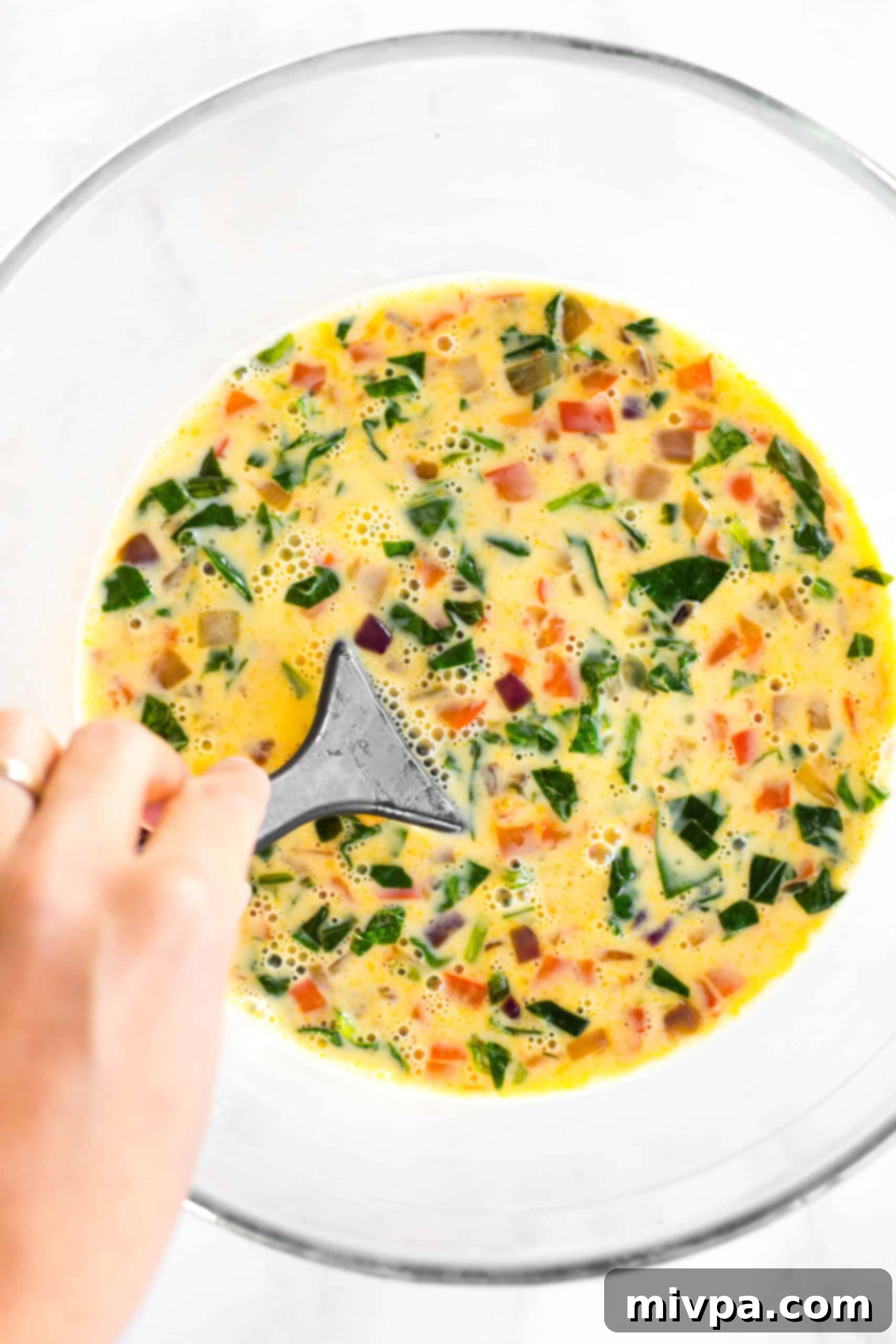 Mini Crustless Quiches (Gluten-Free, Dairy-Free) Mixing cooked vegetables in quiche batter in large glass bowl.