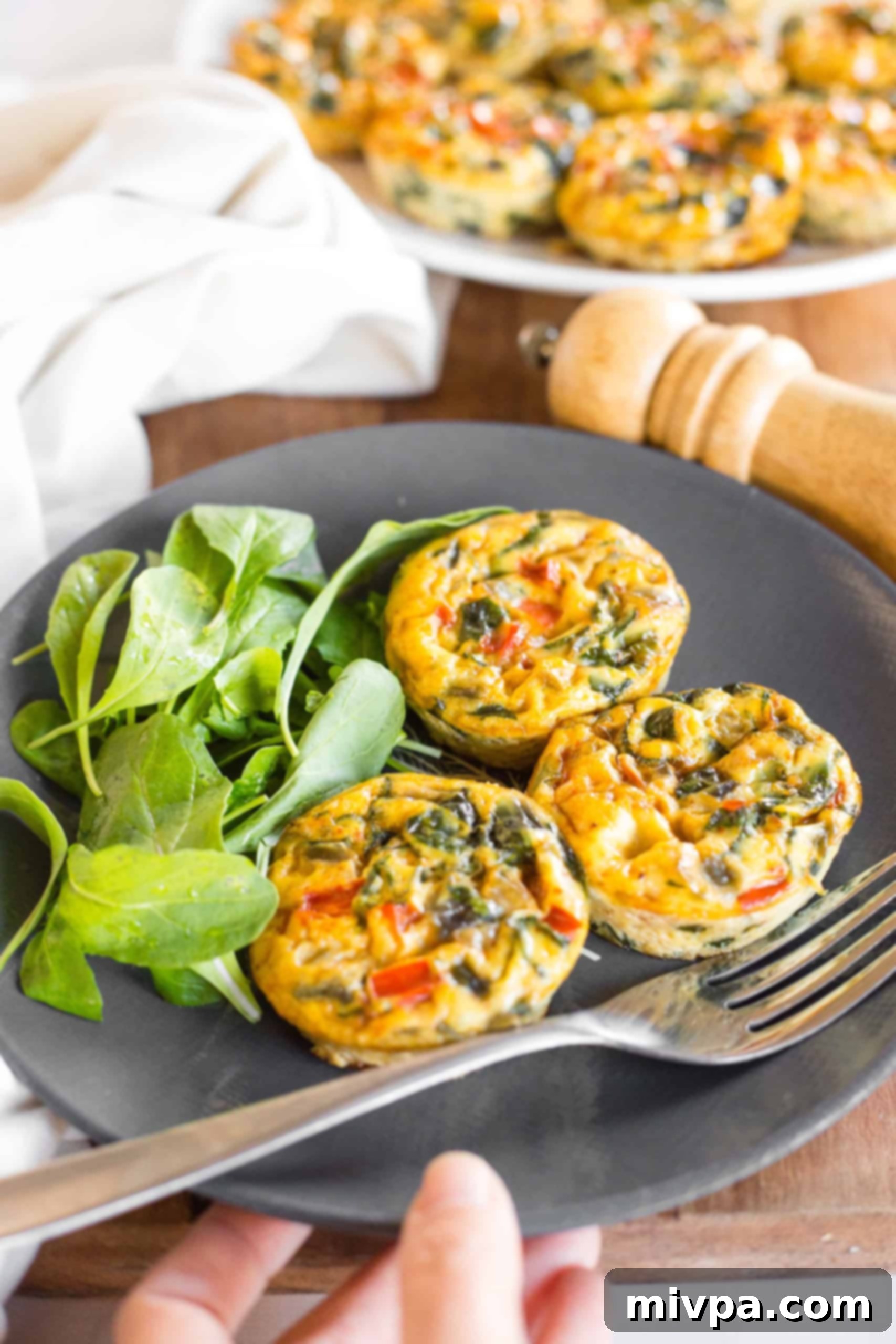Crustless Mini Quiche Recipe without Pastry (Gluten-Free, Dairy-Free) Hand reaching for a plate of crustless mini vegetable quiches and salad on the side.