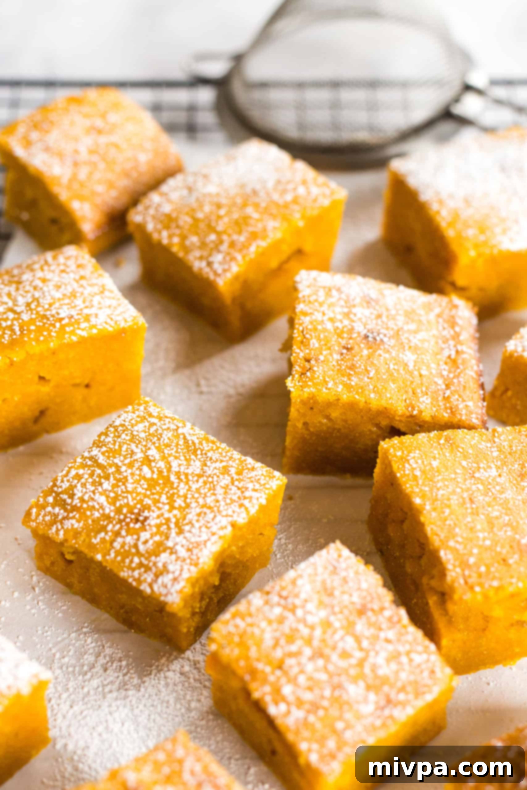 Deliciously moist gluten-free pumpkin bars arranged on a parchment-lined cooling rack, dusted with powdered sugar.