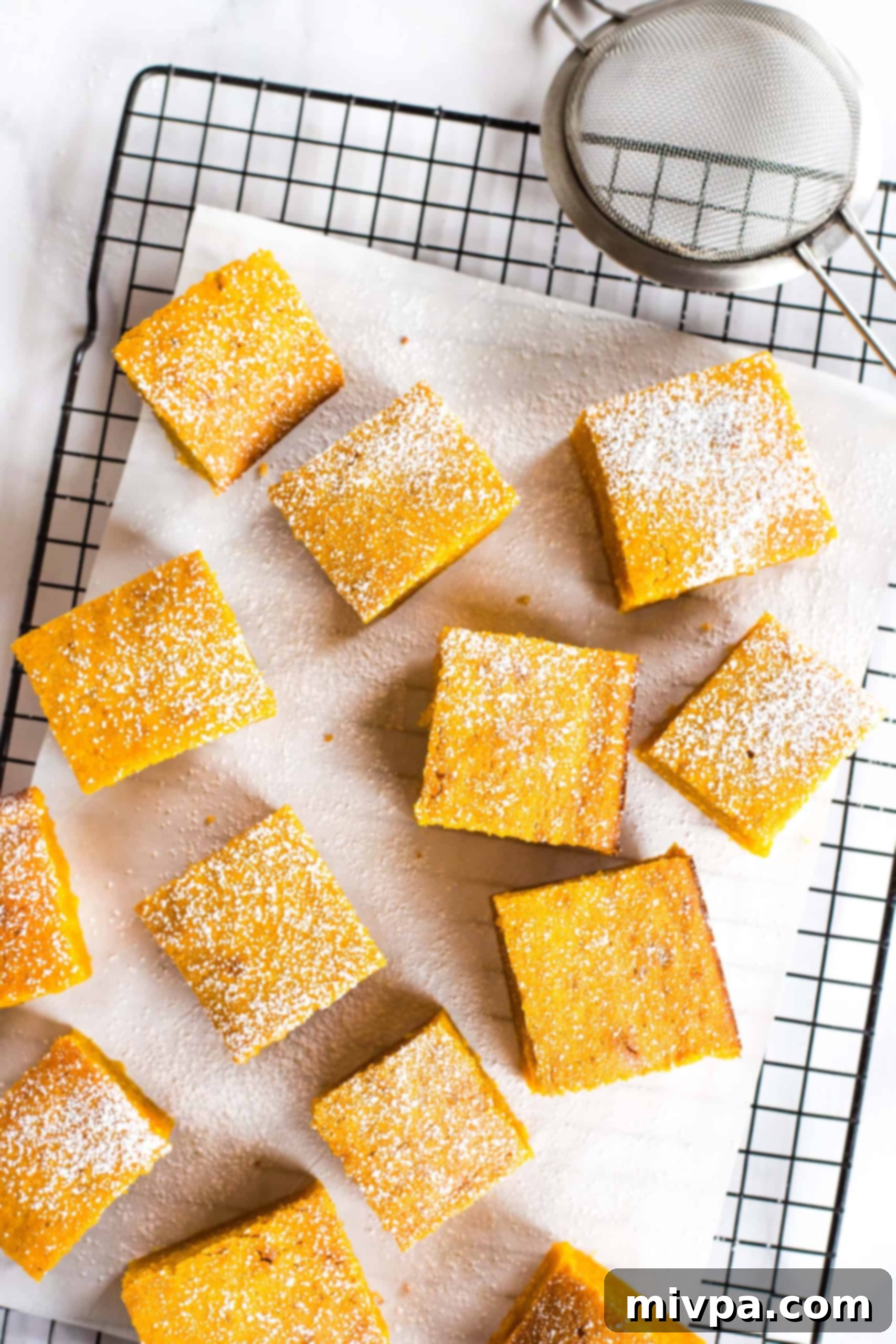 Moist Gluten-Free Pumpkin Bars (Dairy-Free) Gluten-free pumpkin squares sprinkled with powdered sugar on parchment-lined cooling rack.