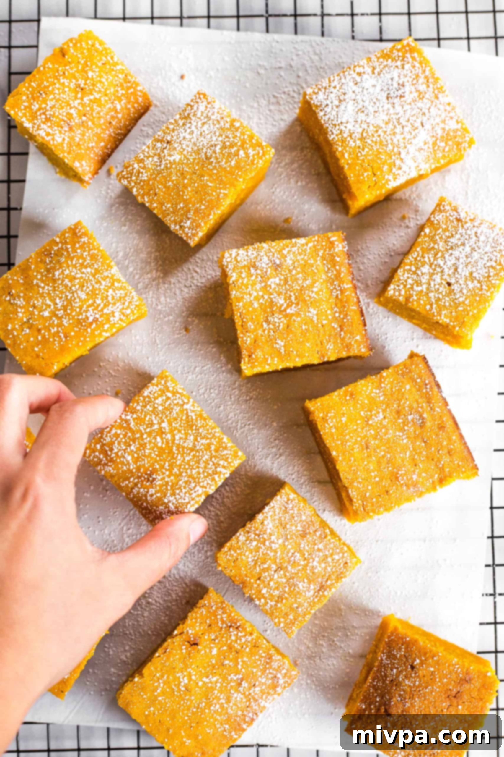 A hand gently reaching for a moist gluten-free pumpkin bar on a cooling rack, signifying its readiness to be enjoyed.