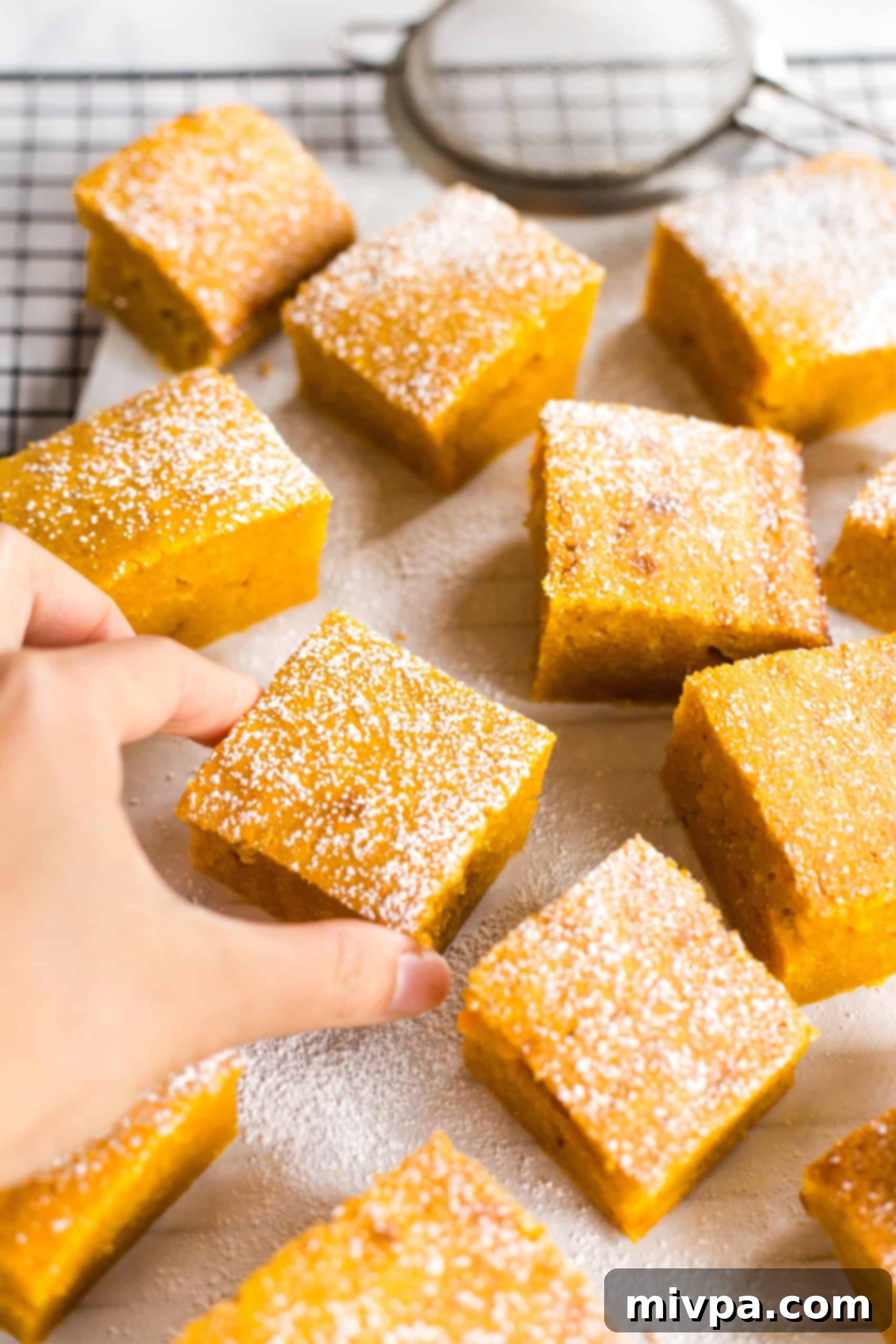 Moist Gluten-Free Pumpkin Squares (Dairy-Free) Hand reaching for pumpkin bars on wire rack.