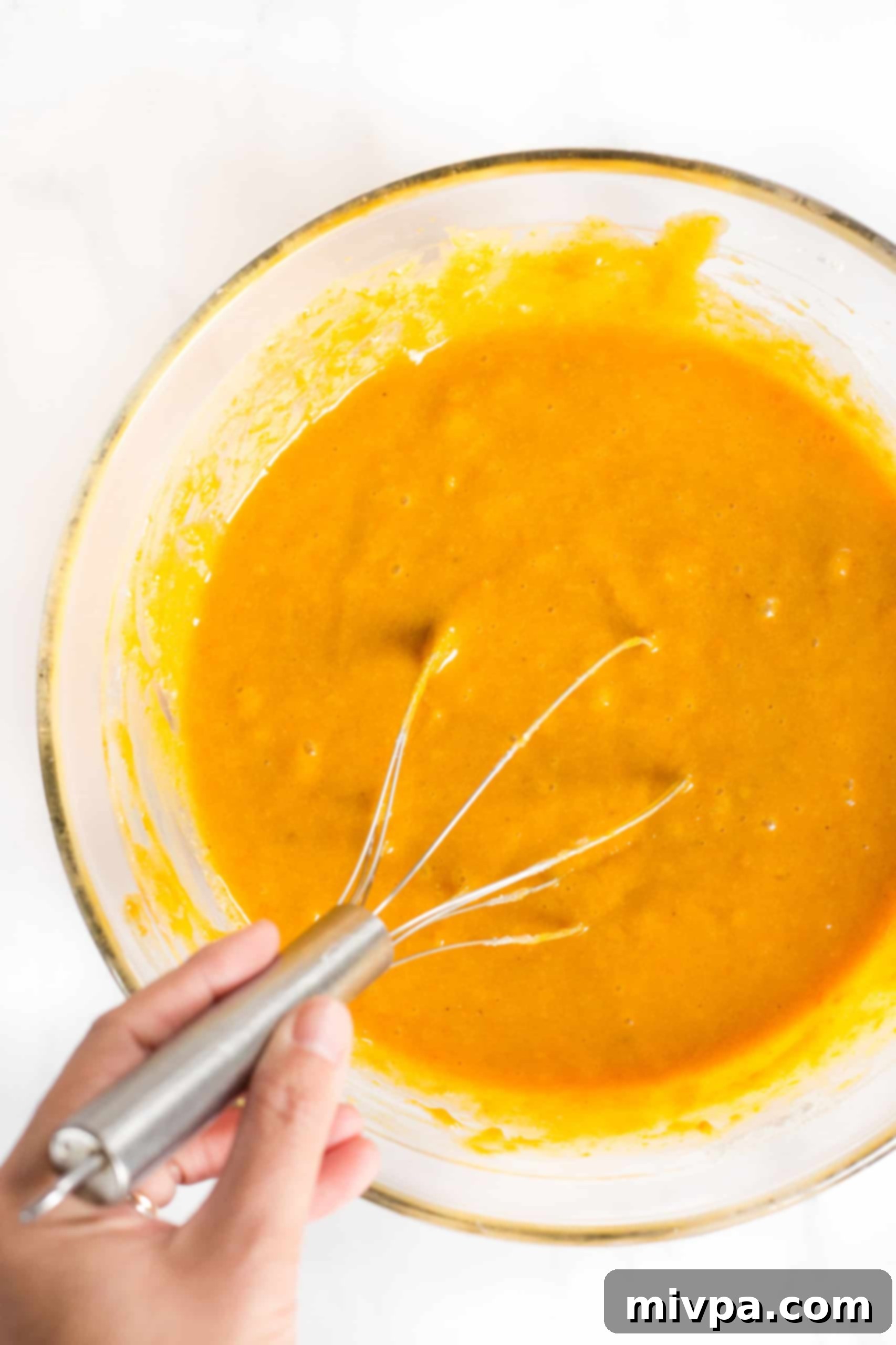 Mixing the dry ingredients into the wet ingredients to form a smooth, pale-orange batter for the pumpkin bars.