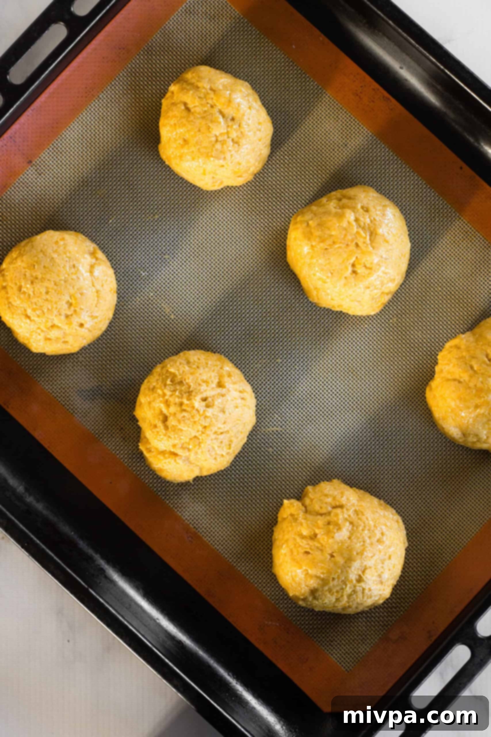 Perfectly spaced pumpkin bagel dough balls resting on a silpat-lined baking sheet, ready for the next step.