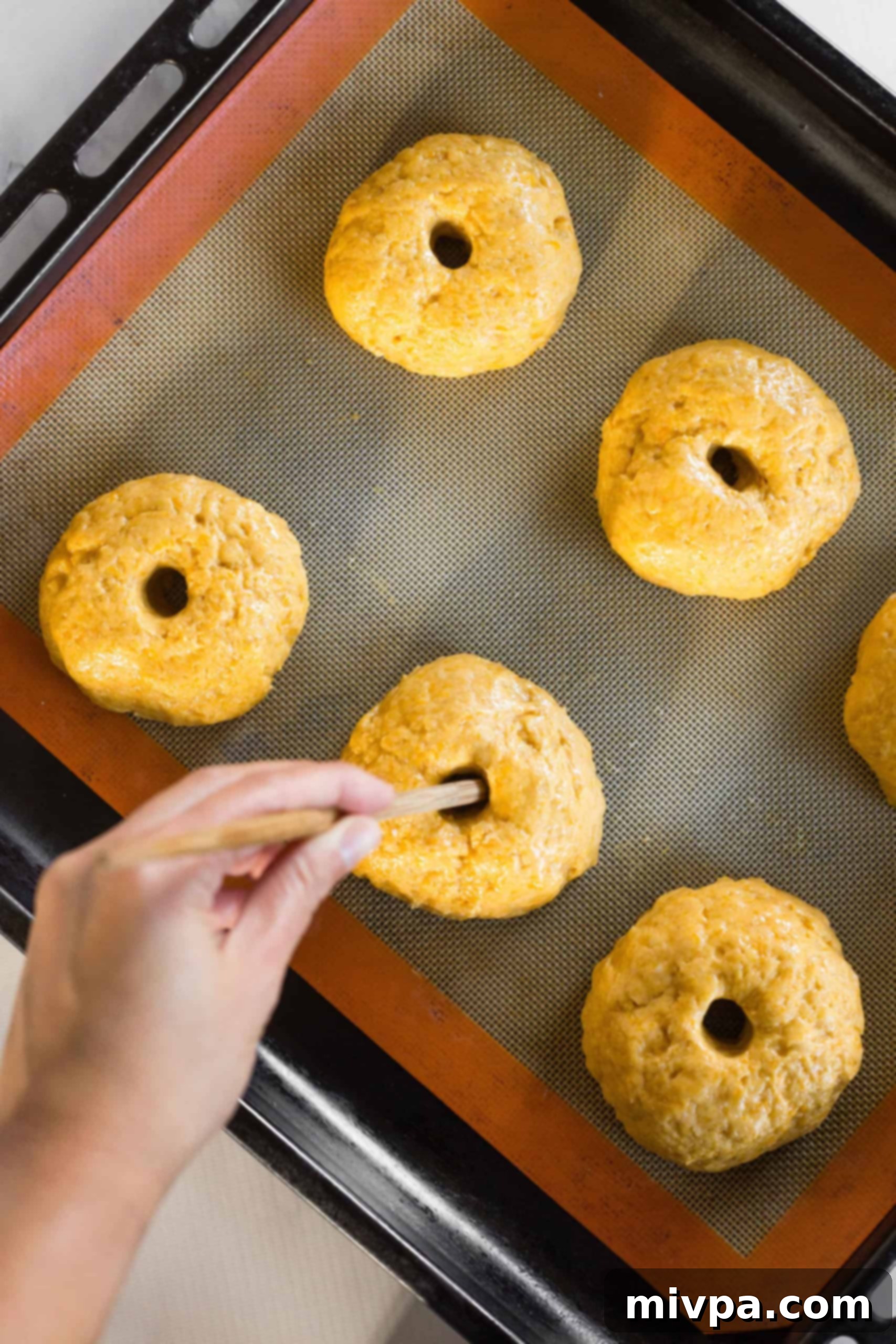 A wooden chopstick being used to expertly poke and shape holes in the pumpkin bagel dough, creating the classic bagel form.