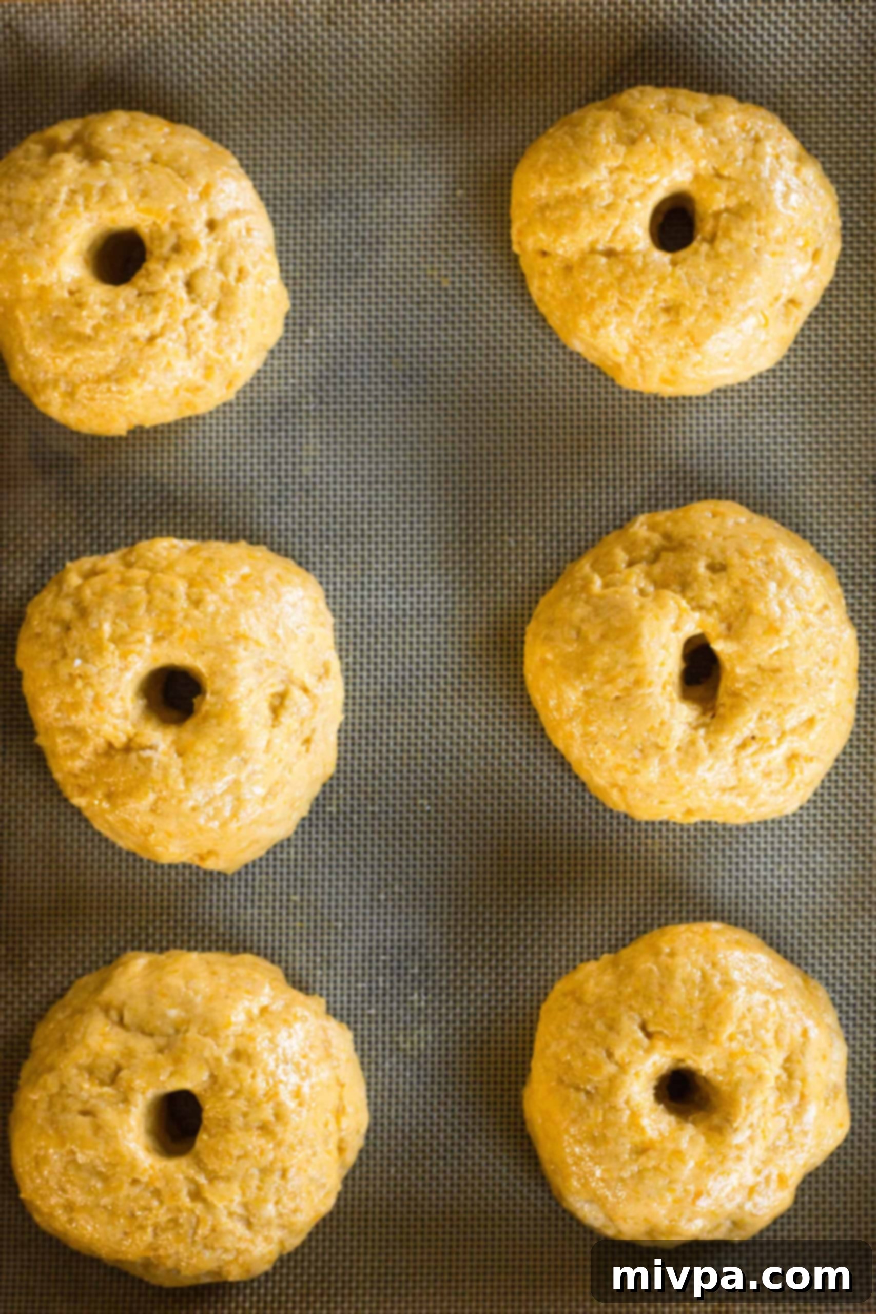 Gluten-free pumpkin bagel dough gently rising on a silpat-lined baking sheet, showing a slight increase in volume.
