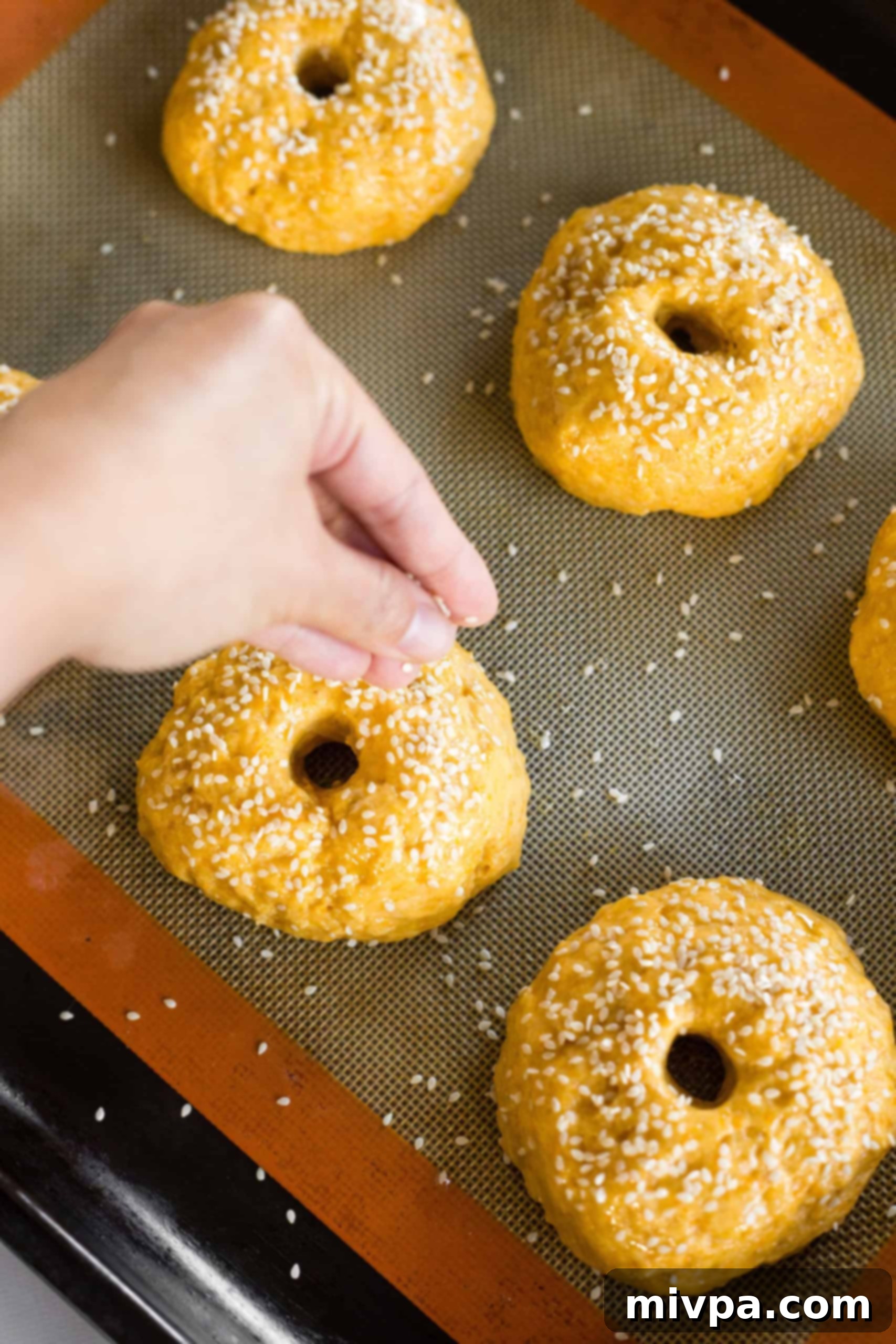 White sesame seeds being sprinkled over the tops of gluten-free pumpkin bagel dough, ready for baking.
