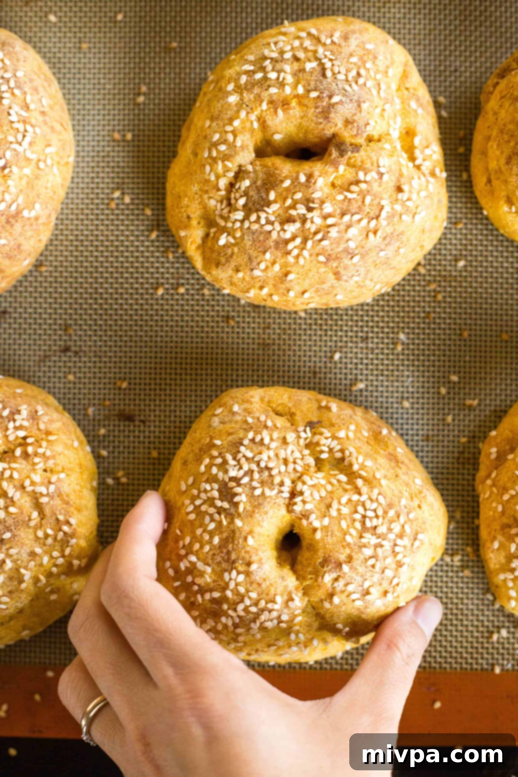 A hand reaching for a freshly-baked, golden-brown pumpkin bagel, hot and ready from the oven.