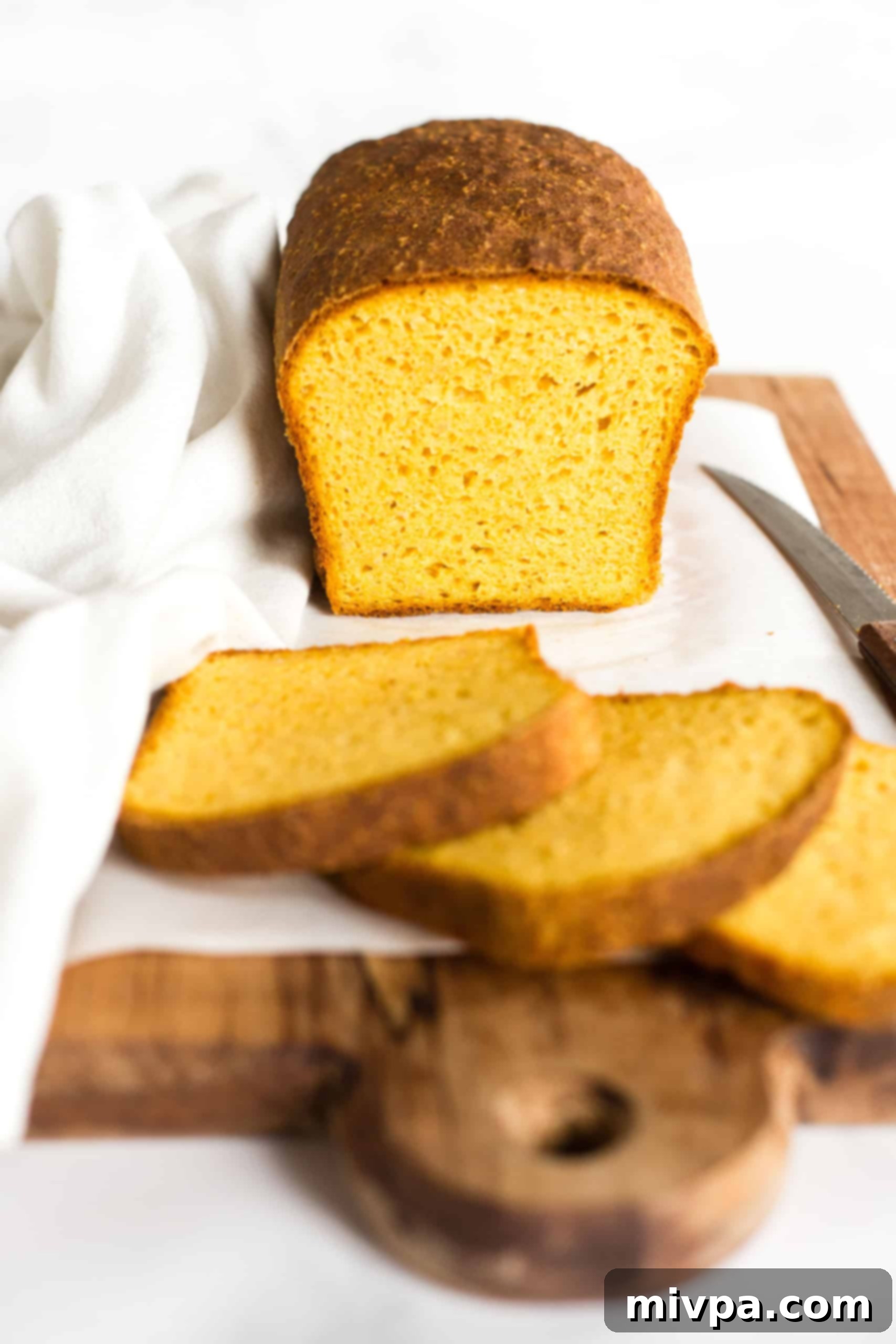 Sliced loaf of gluten-free pumpkin yeast bread on parchment-lined board.