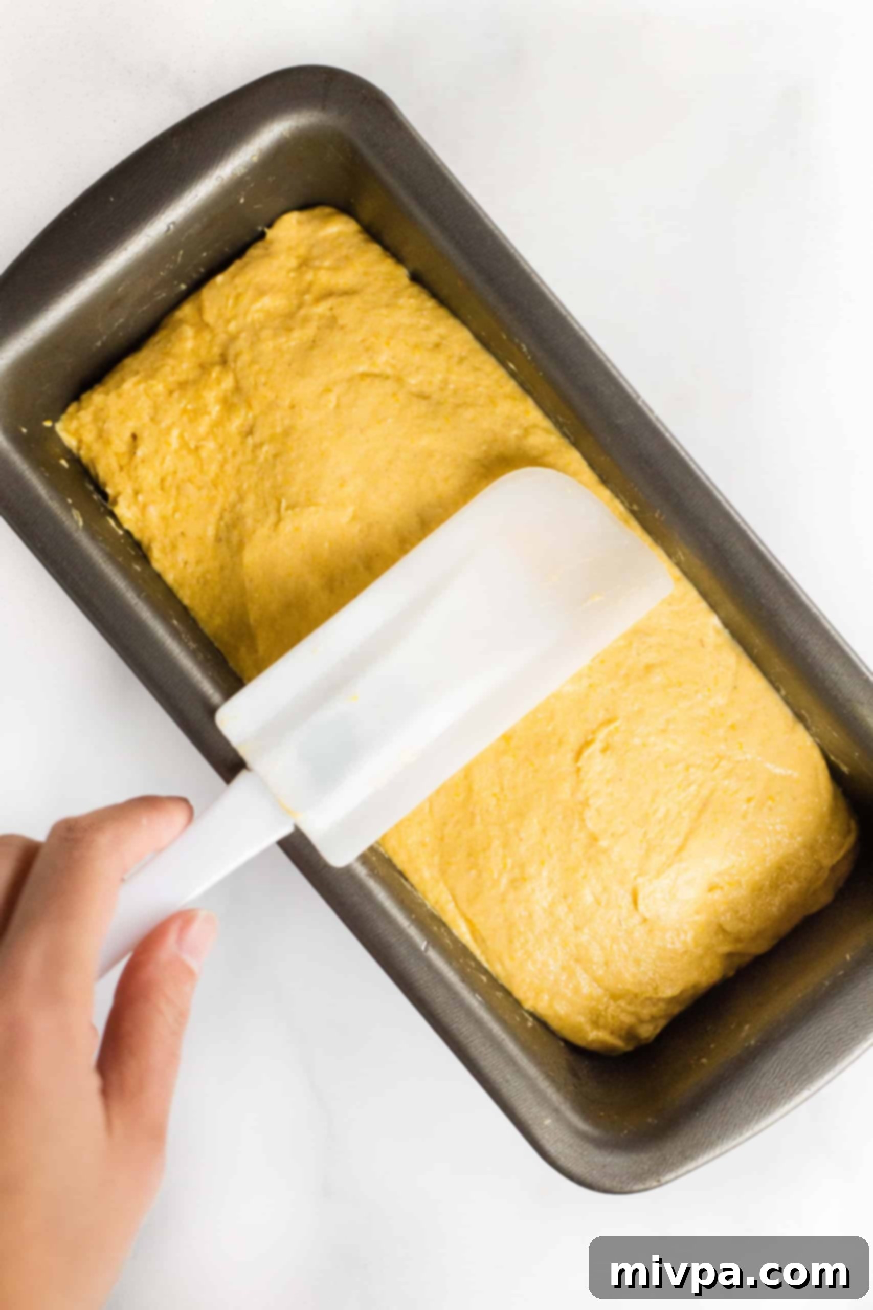 Smoothing out top of pumpkin bread dough with wet spatula.