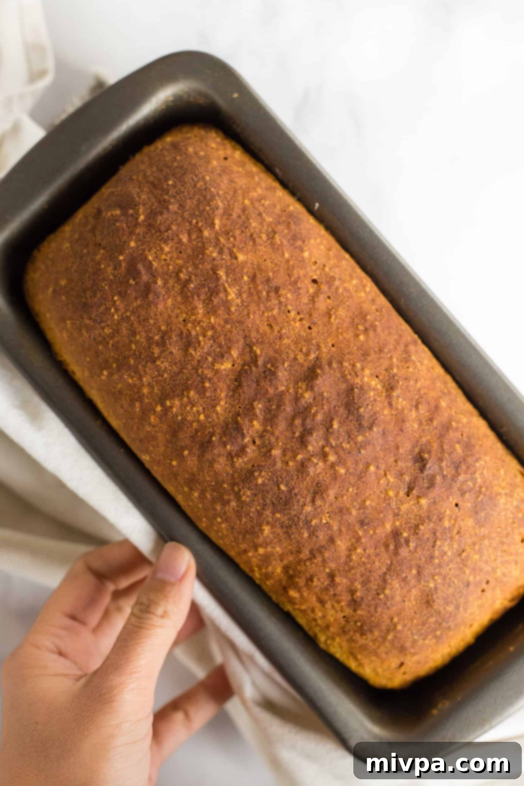 A freshly baked loaf of pumpkin yeast bread in metal pan.
