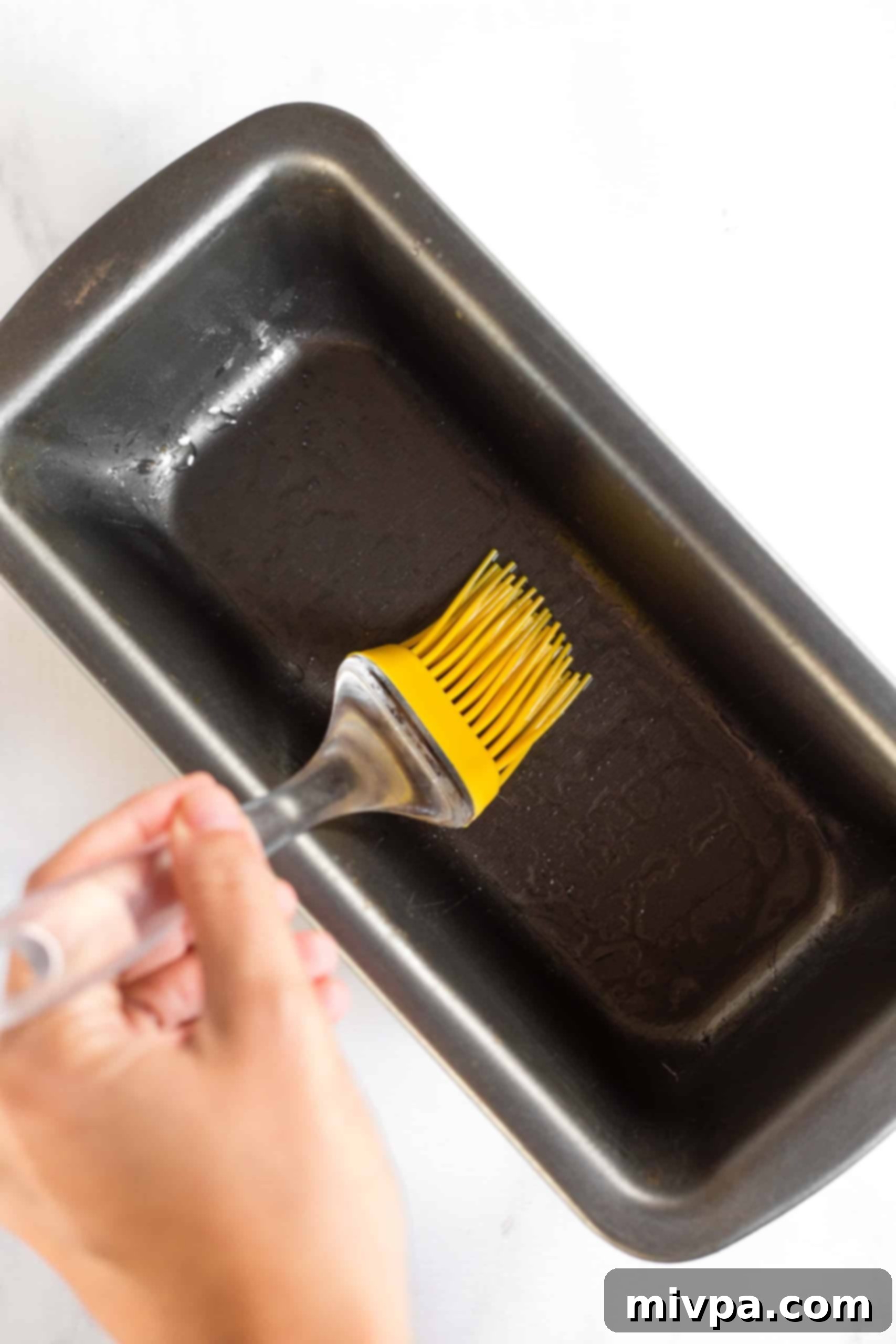 Using silicon brush to grease metal loaf pan.