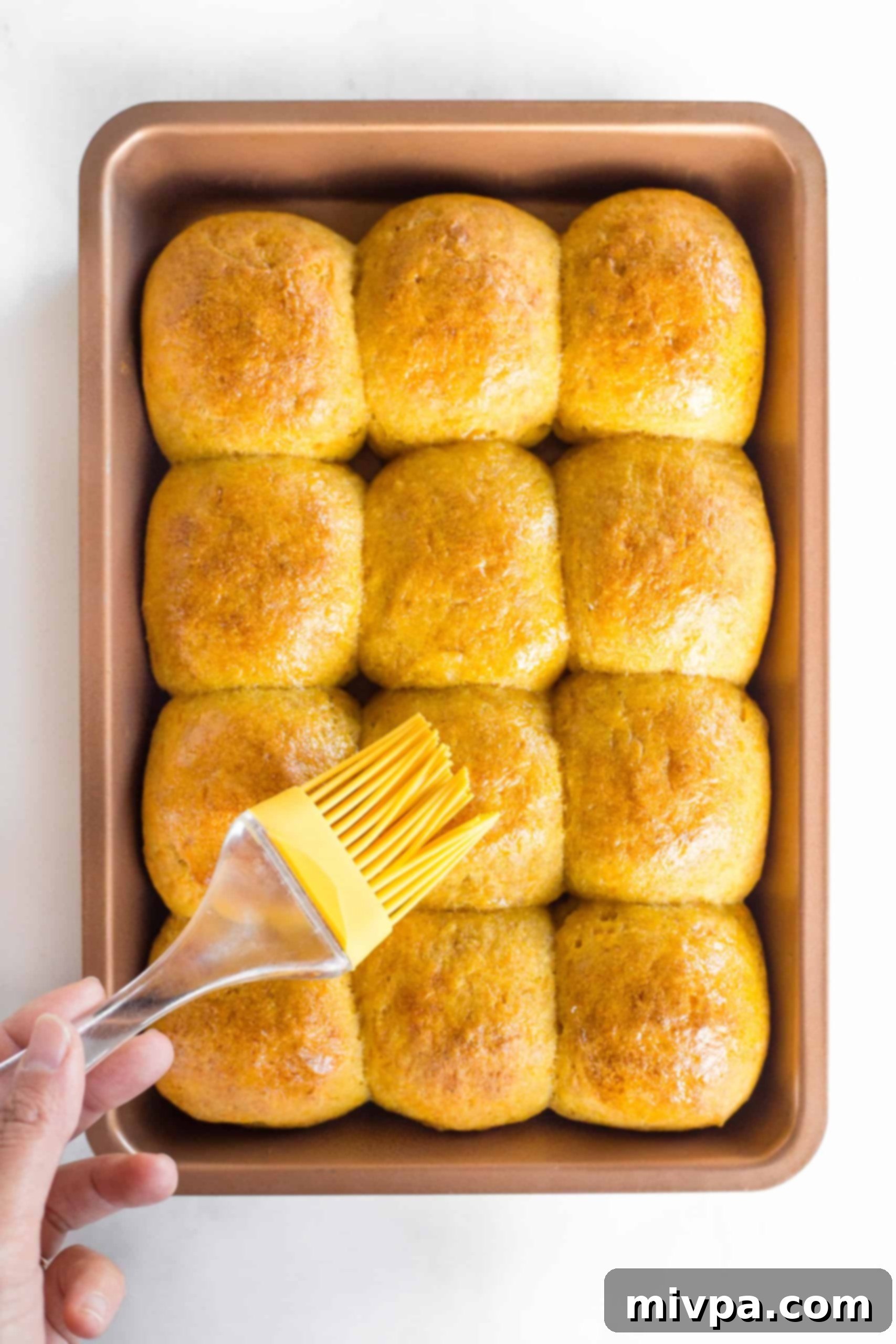 Brushing tops of pumpkin dinner rolls with oil.