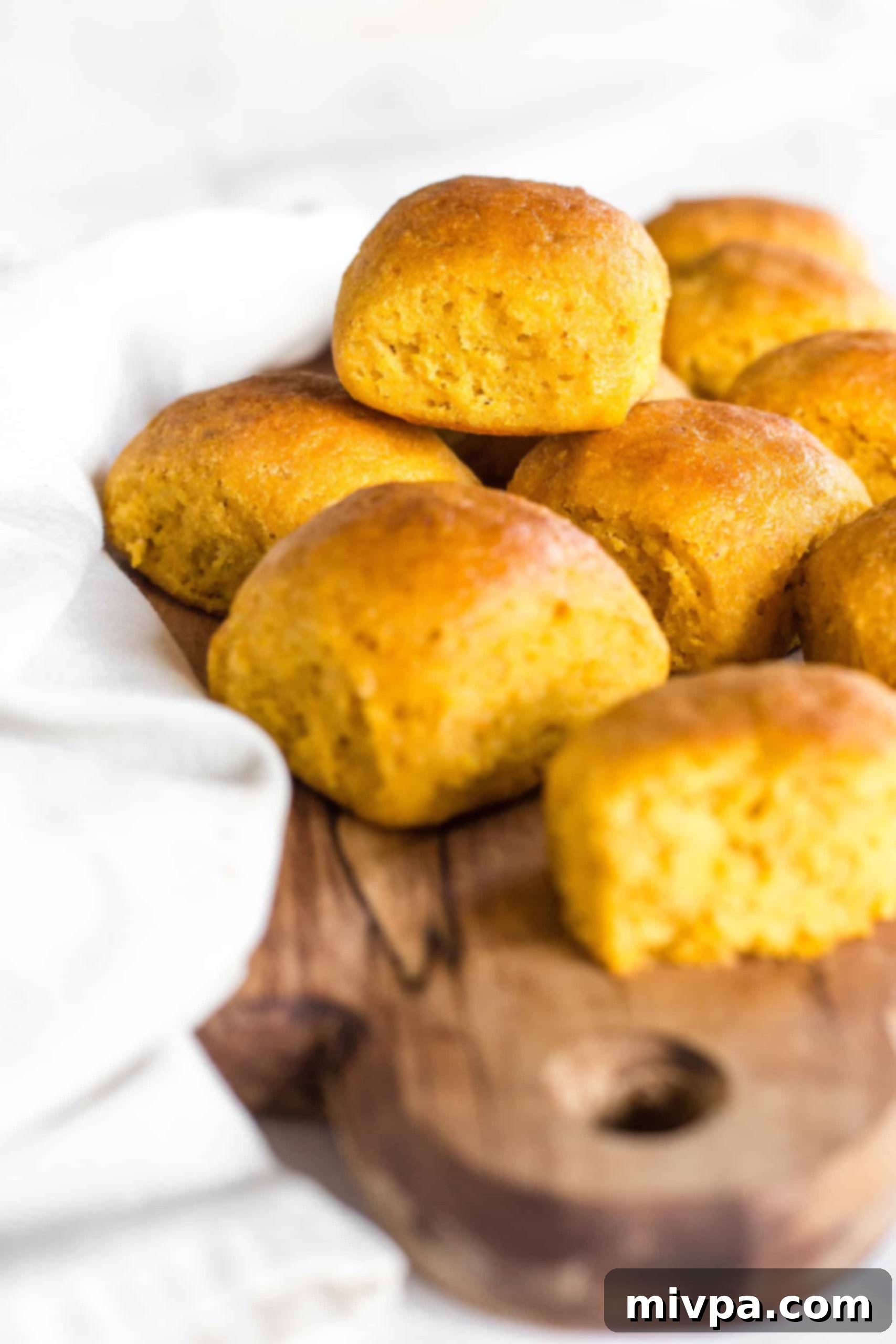 A stack of pumpkin dinner rolls on wooden board.