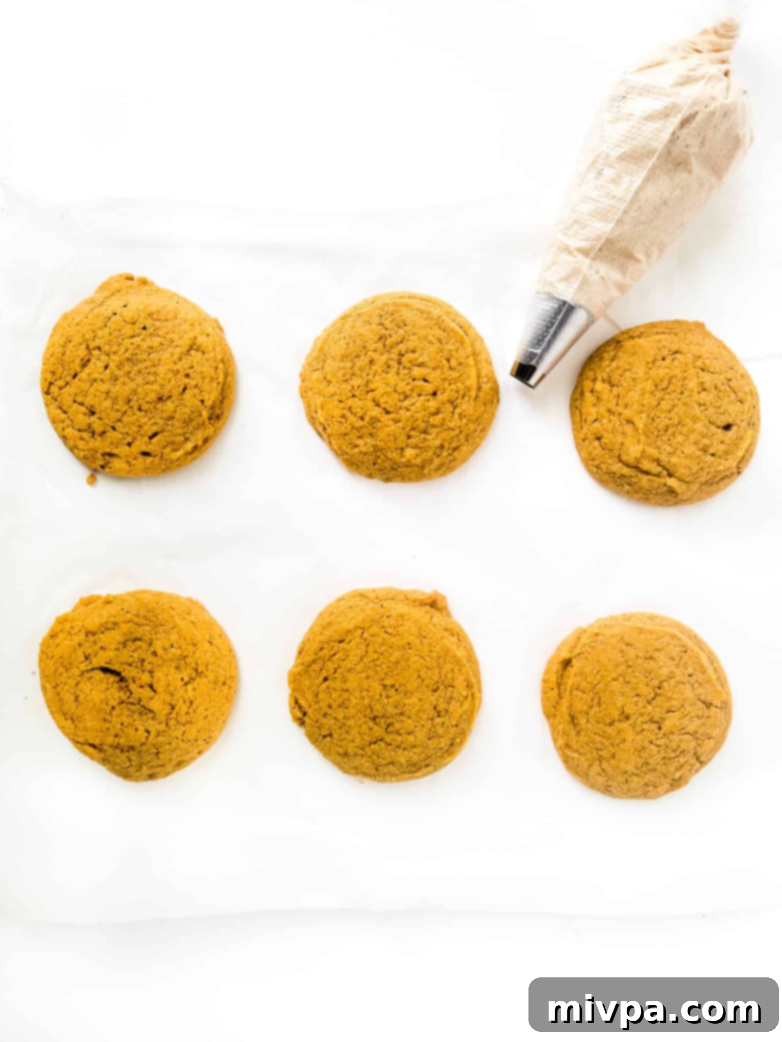 Gluten-Free Crumbl Cookies (Dairy-Free) Freshly baked gluten-free pumpkin cookies with a piping bag filled with frosting.