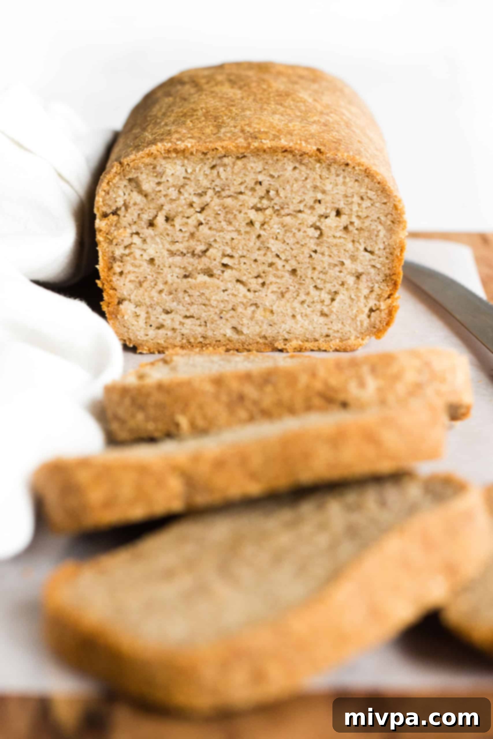 Gluten-Free Whole Grain Bread (Dairy-Free, Vegan) A half-sliced loaf of hearty gluten-free whole grain bread on a wooden board.