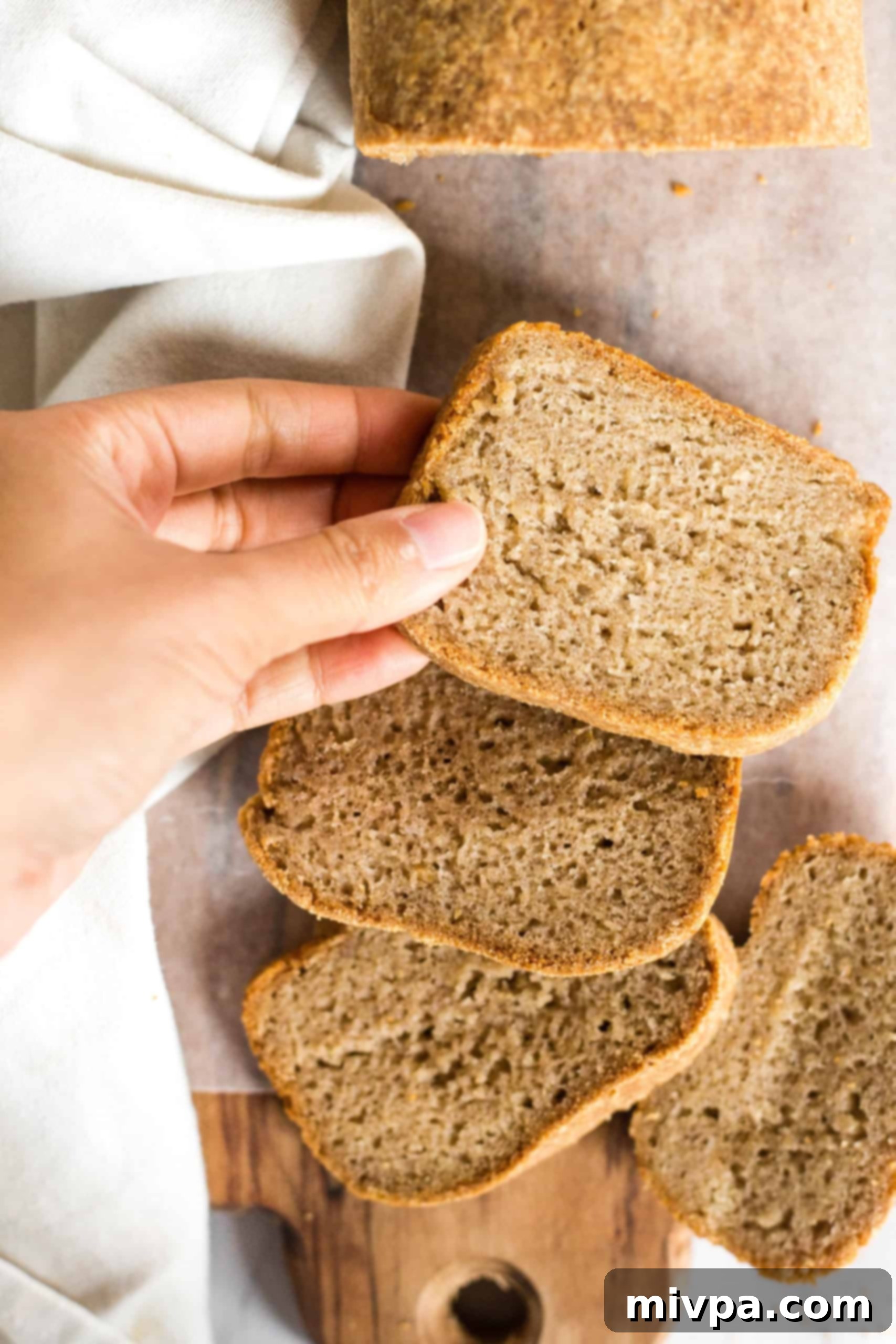 Gluten-Free Brown Bread (Dairy-Free, Vegan) Hand reaching for a slice of freshly baked gluten-free whole grain bread.