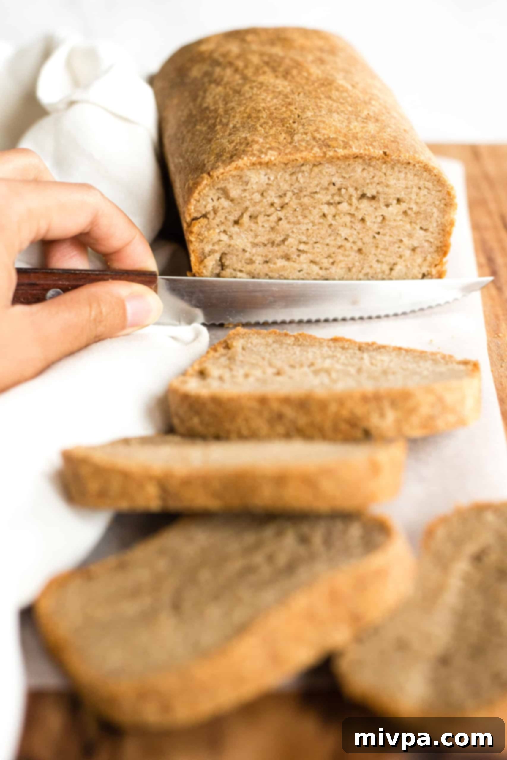Gluten-Free Whole Grain Bread (Dairy-Free, Vegan) Slicing into a freshly baked loaf of gluten-free brown bread on a cutting board.