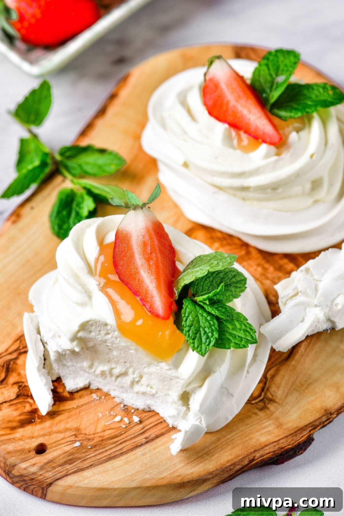 Half-eaten mini pavlova nests on wooden board.