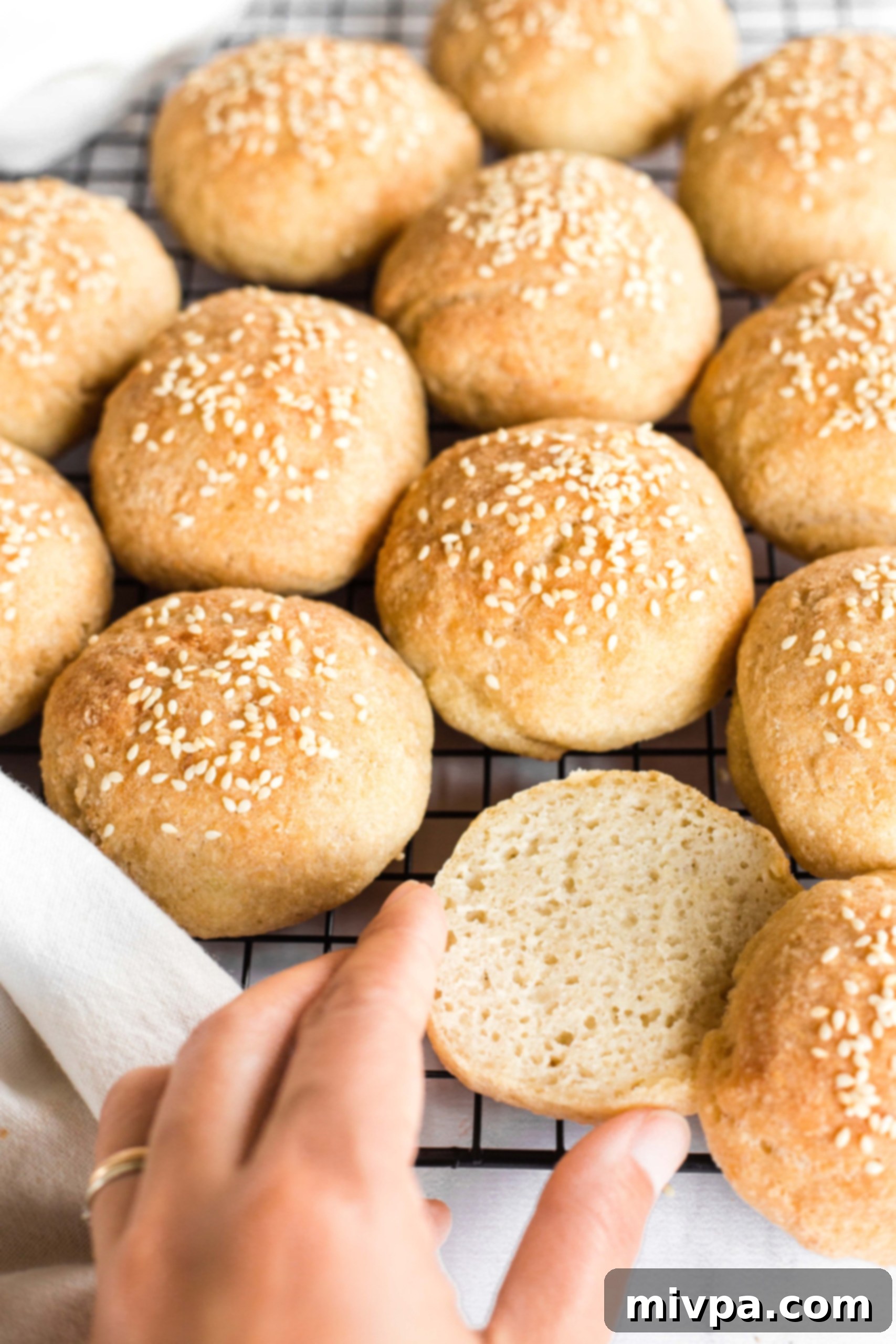 Hand reaching for a gluten-free slider bun on a wire rack, highlighting its soft texture.