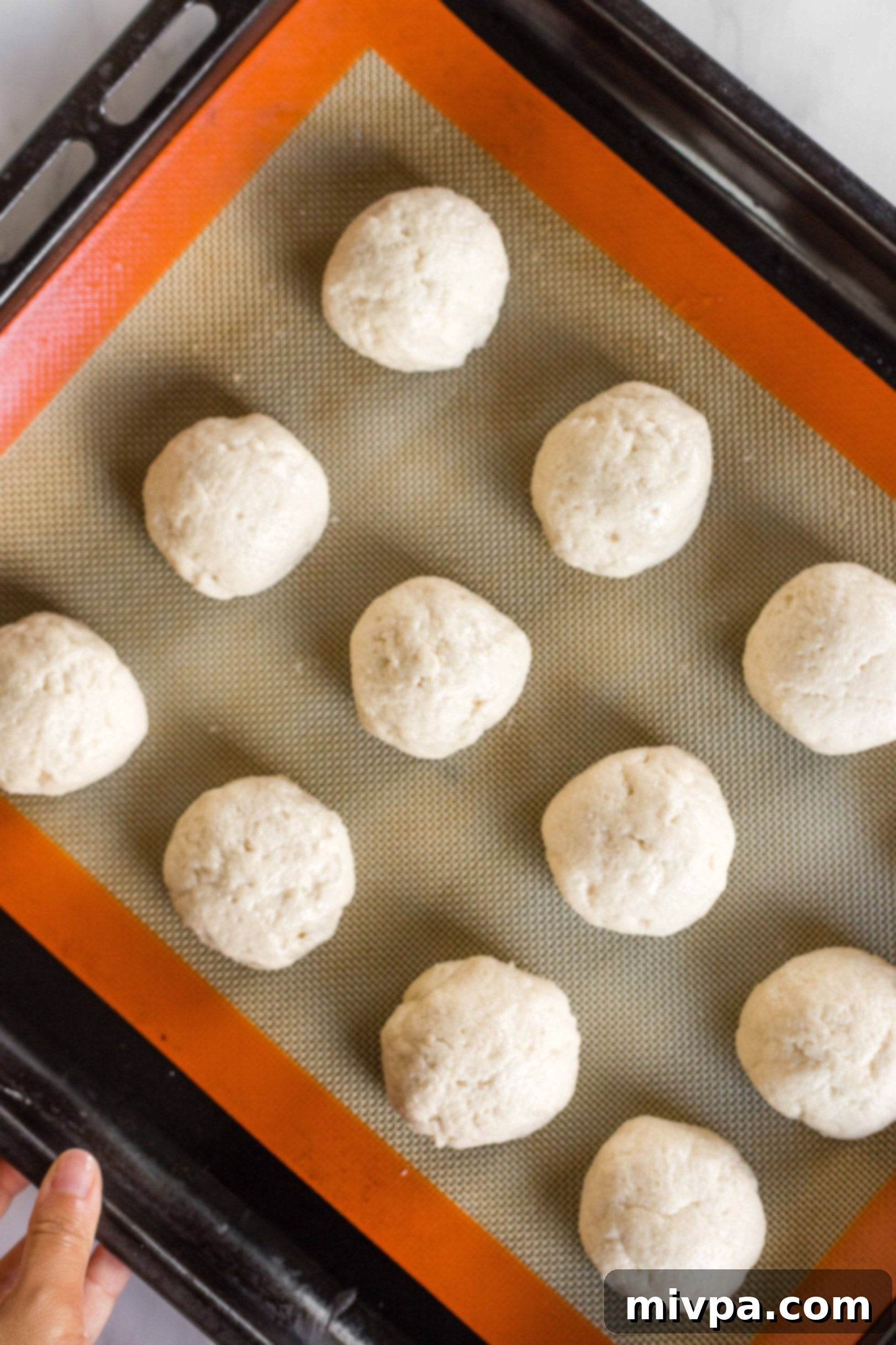 Uniform balls of gluten-free slider bun dough arranged on a silpat-lined baking sheet.
