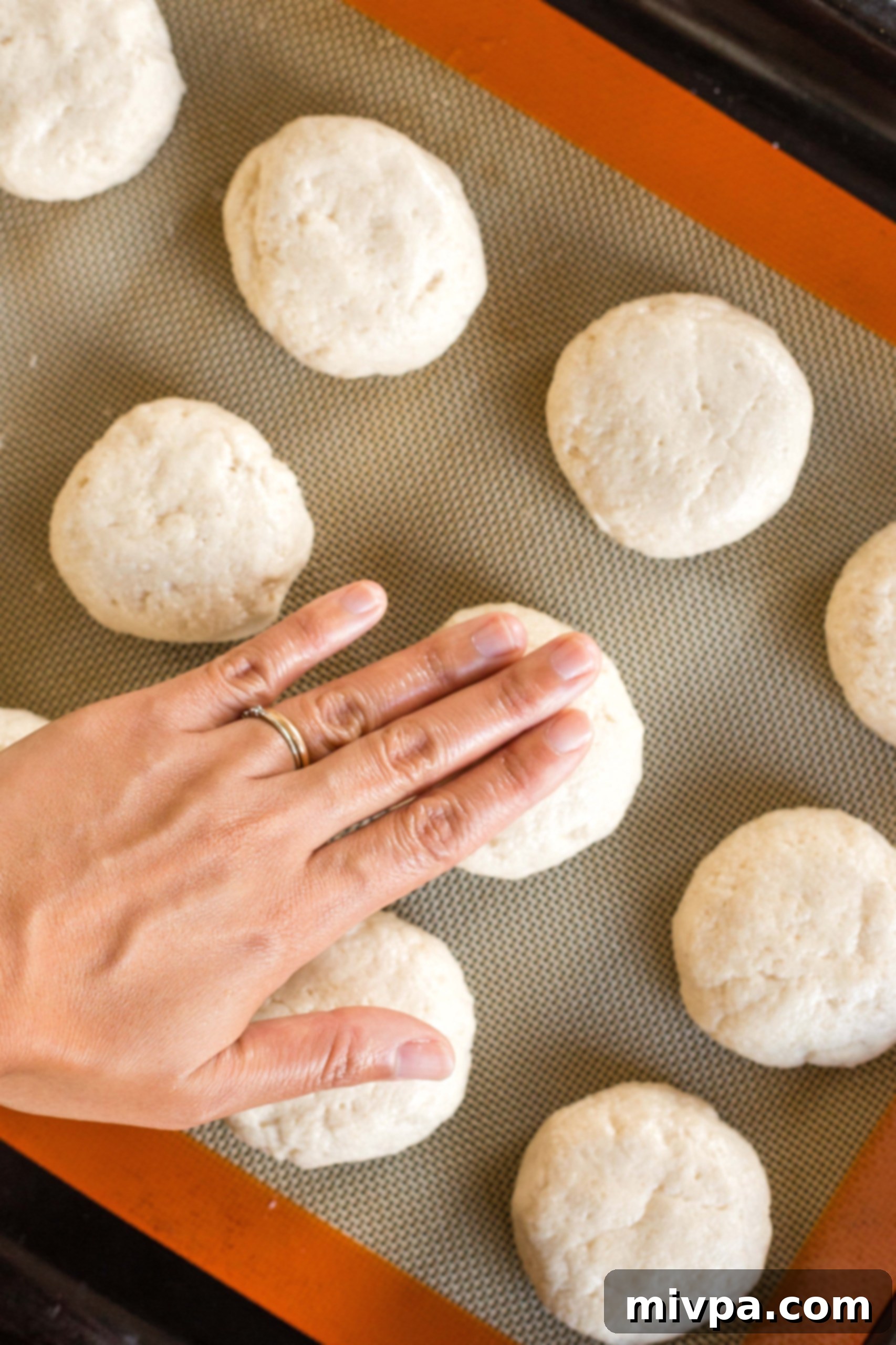 Fingers gently flattening balls of dough on a baking sheet to shape them.