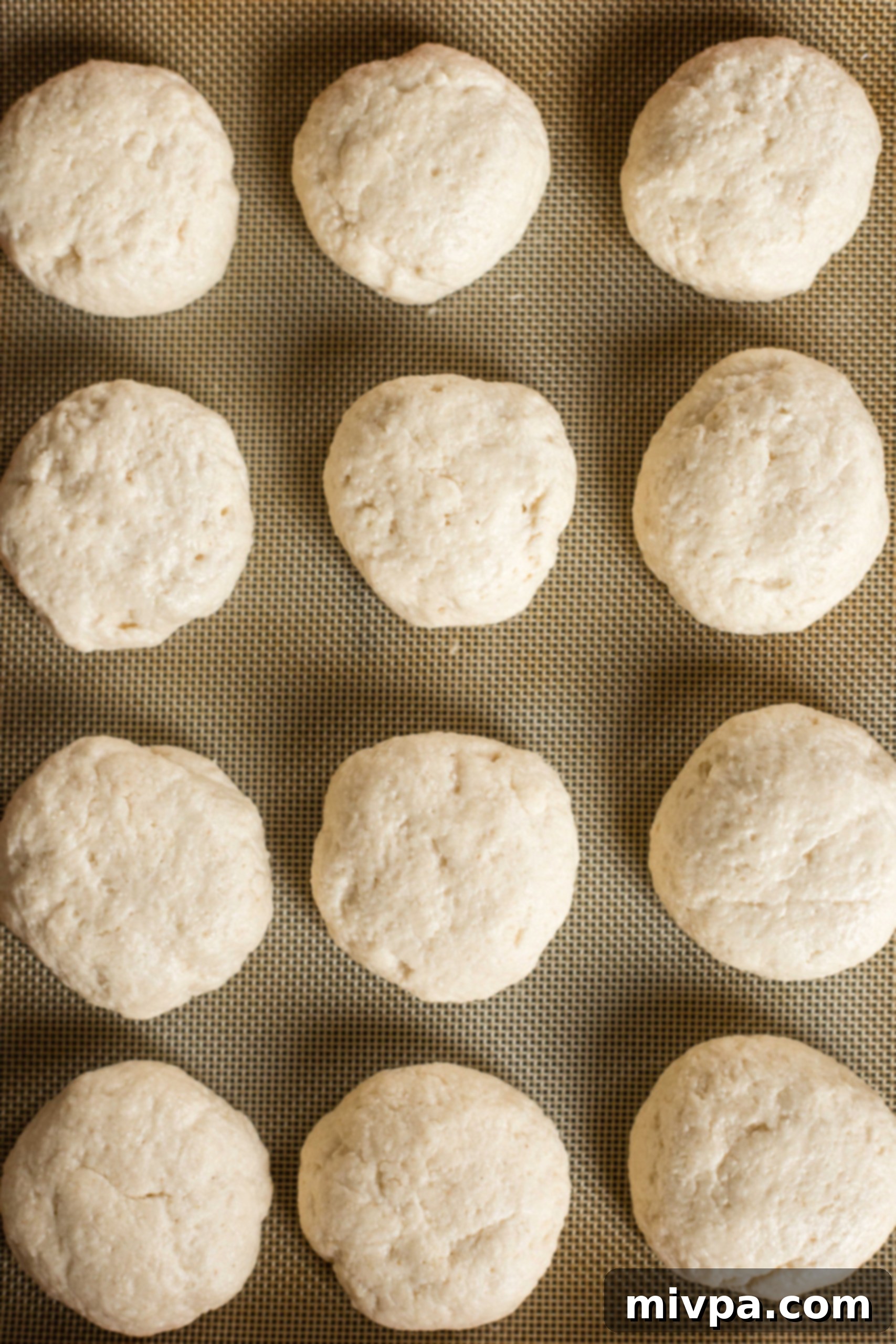 Dough balls visibly rising on a silpat-lined baking sheet, covered and warm.