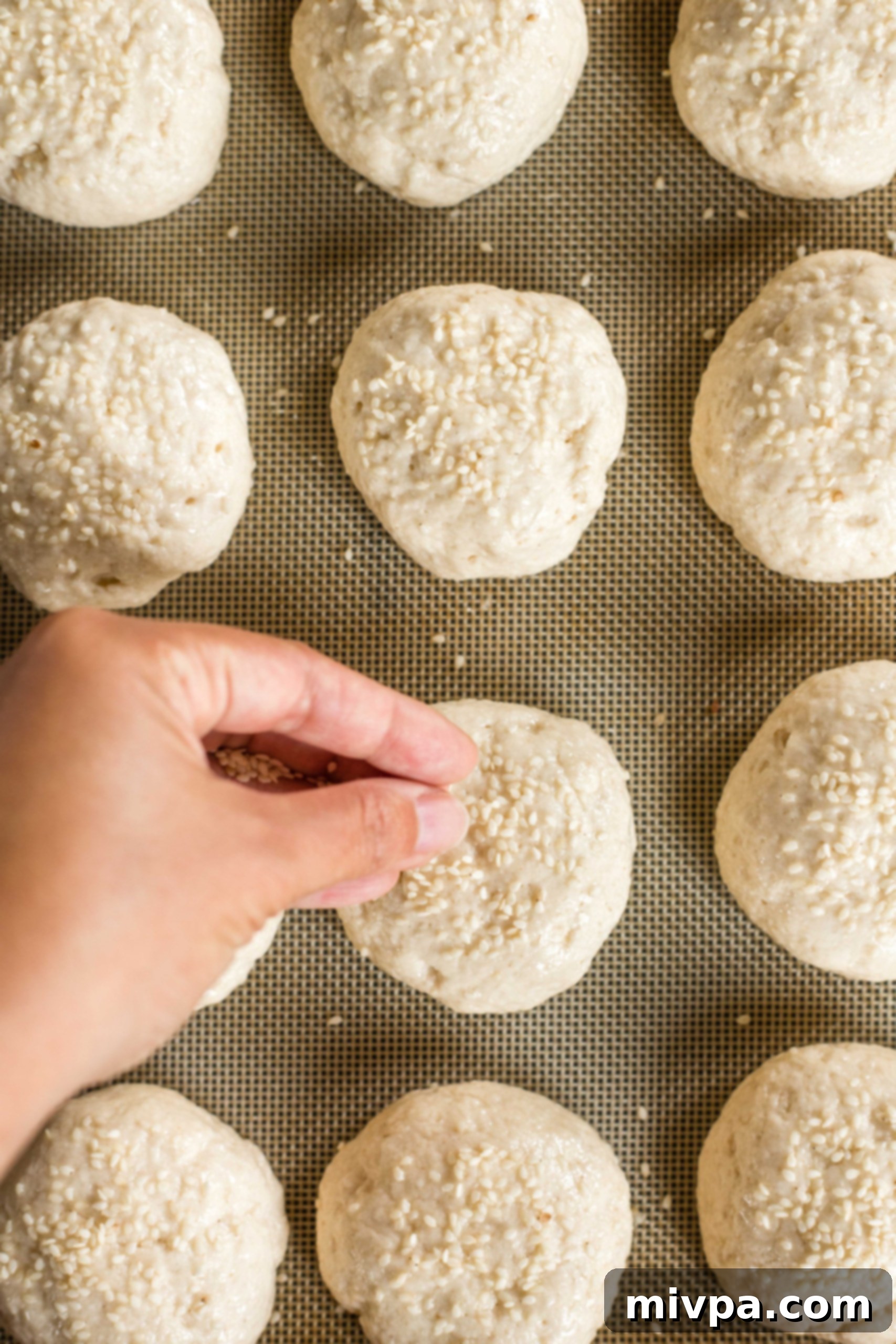 Hand sprinkling sesame seeds over gluten-free slider bun dough before baking.