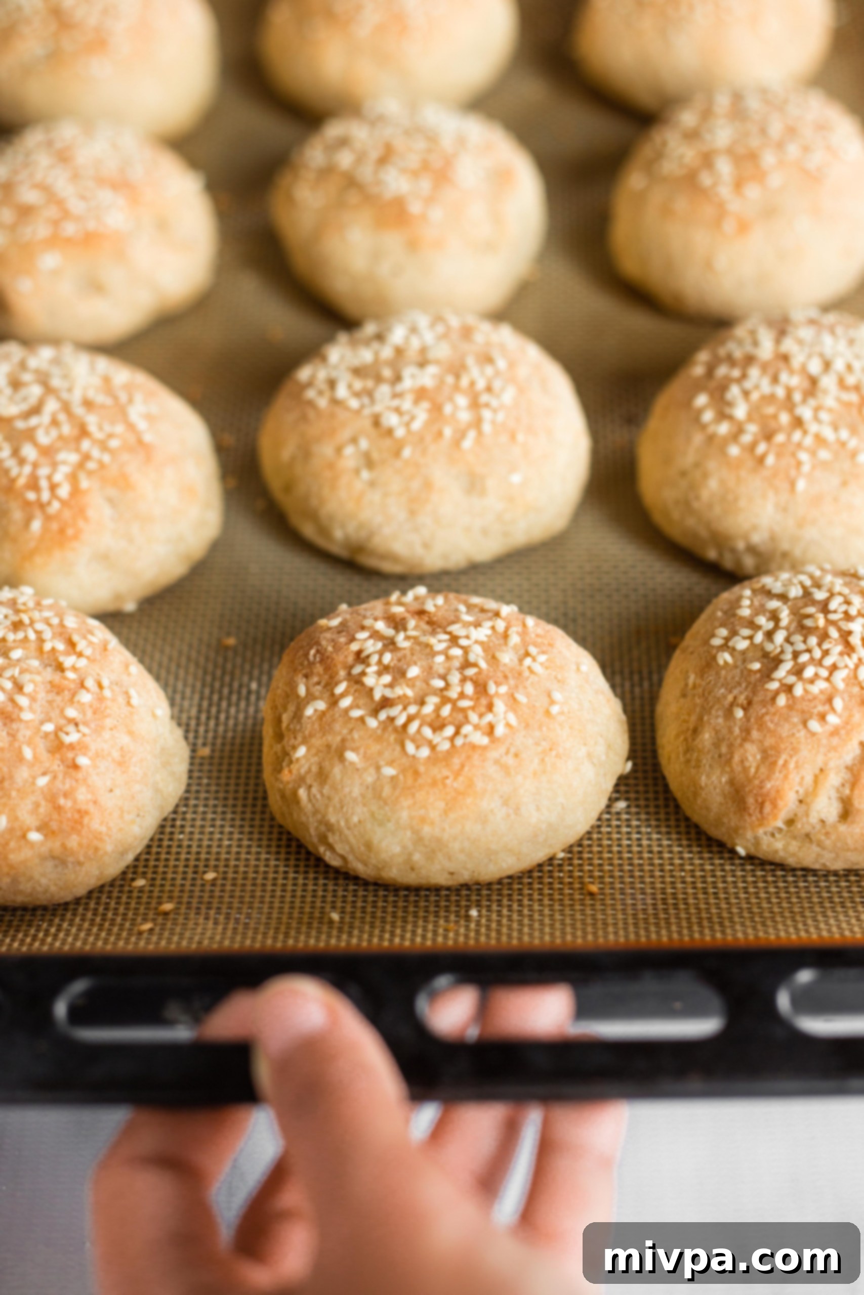 Holding a large baking sheet filled with freshly baked, golden-brown gluten-free slider buns.