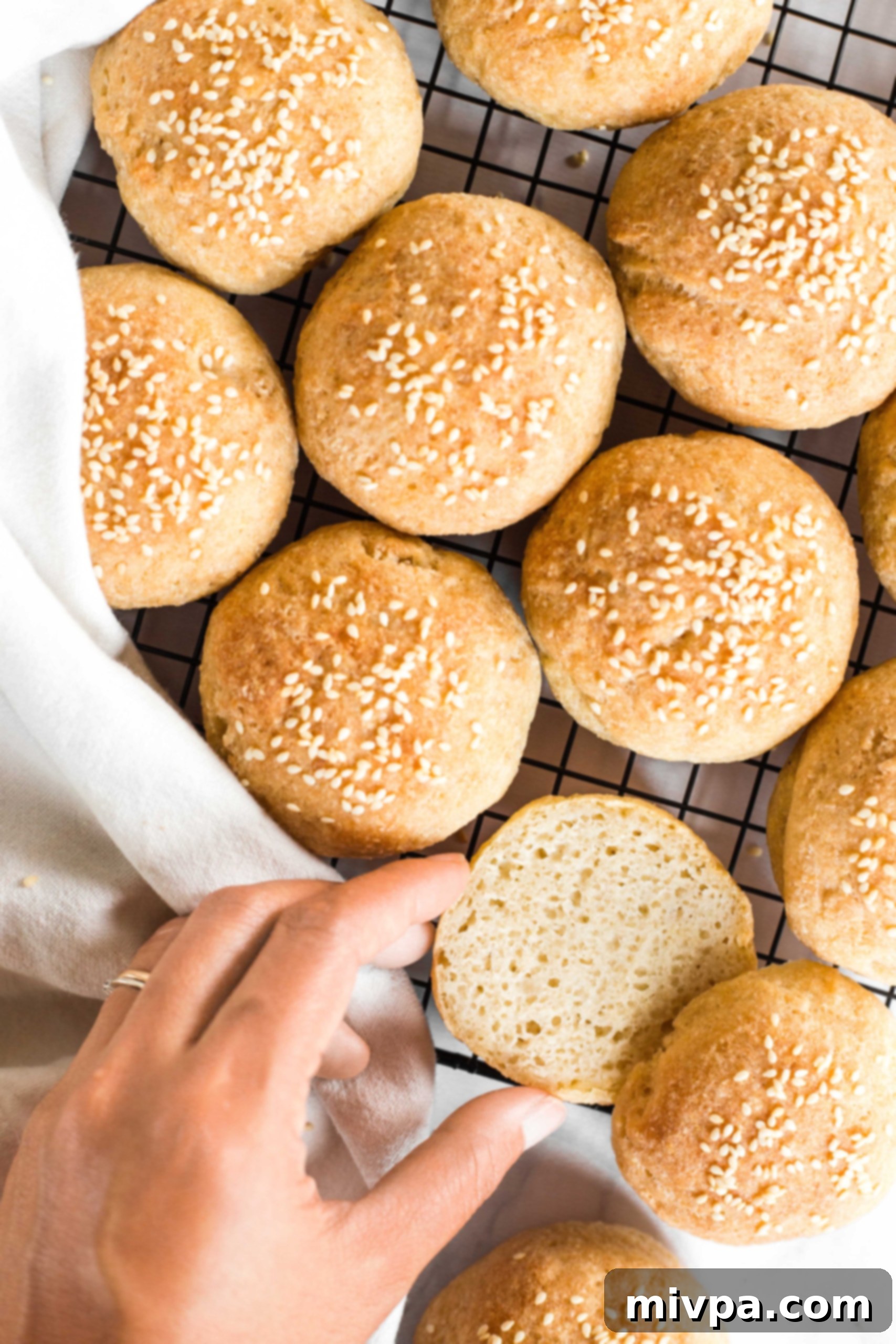 Hand reaching for a perfectly sliced mini slider bun on a wire rack, ready to be filled.
