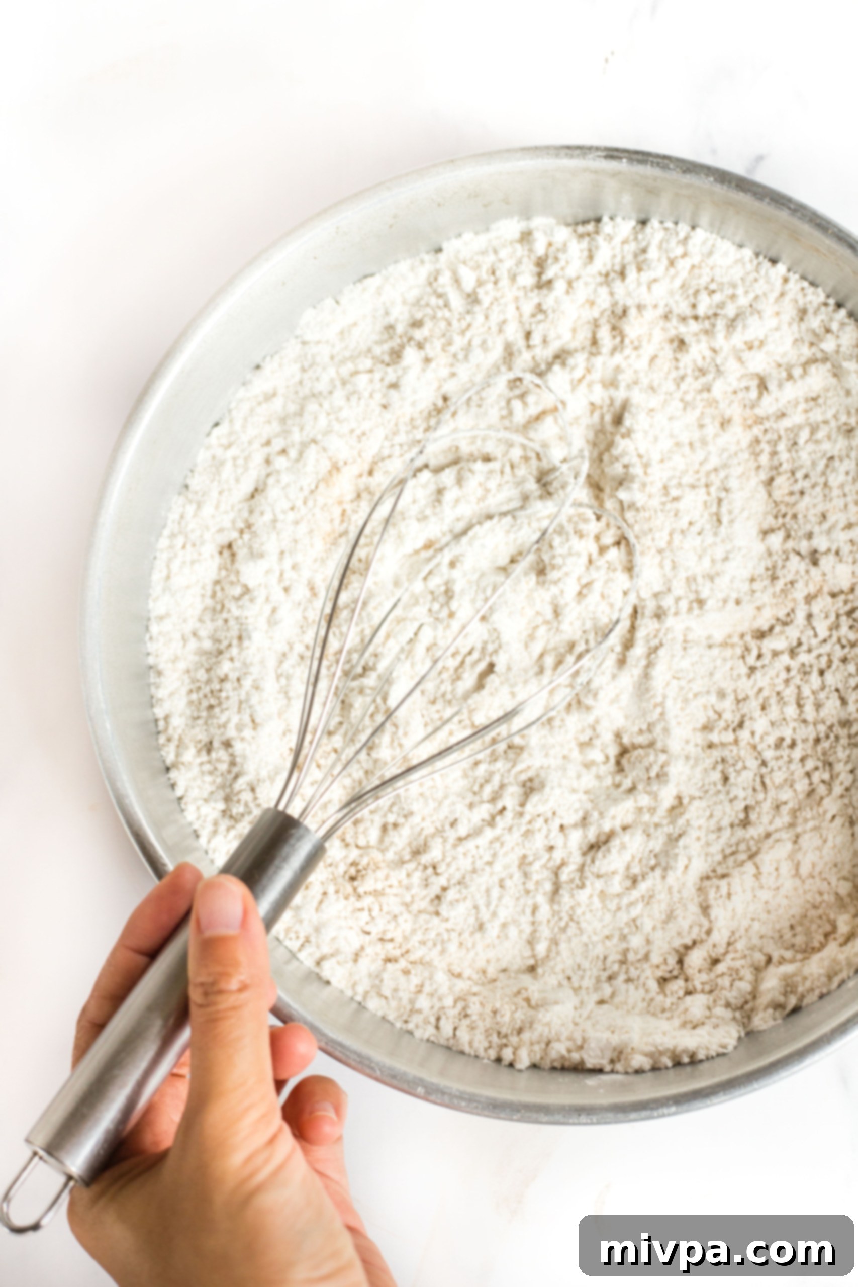 A whisk combining flour mixture in a metal bowl, ensuring even distribution.