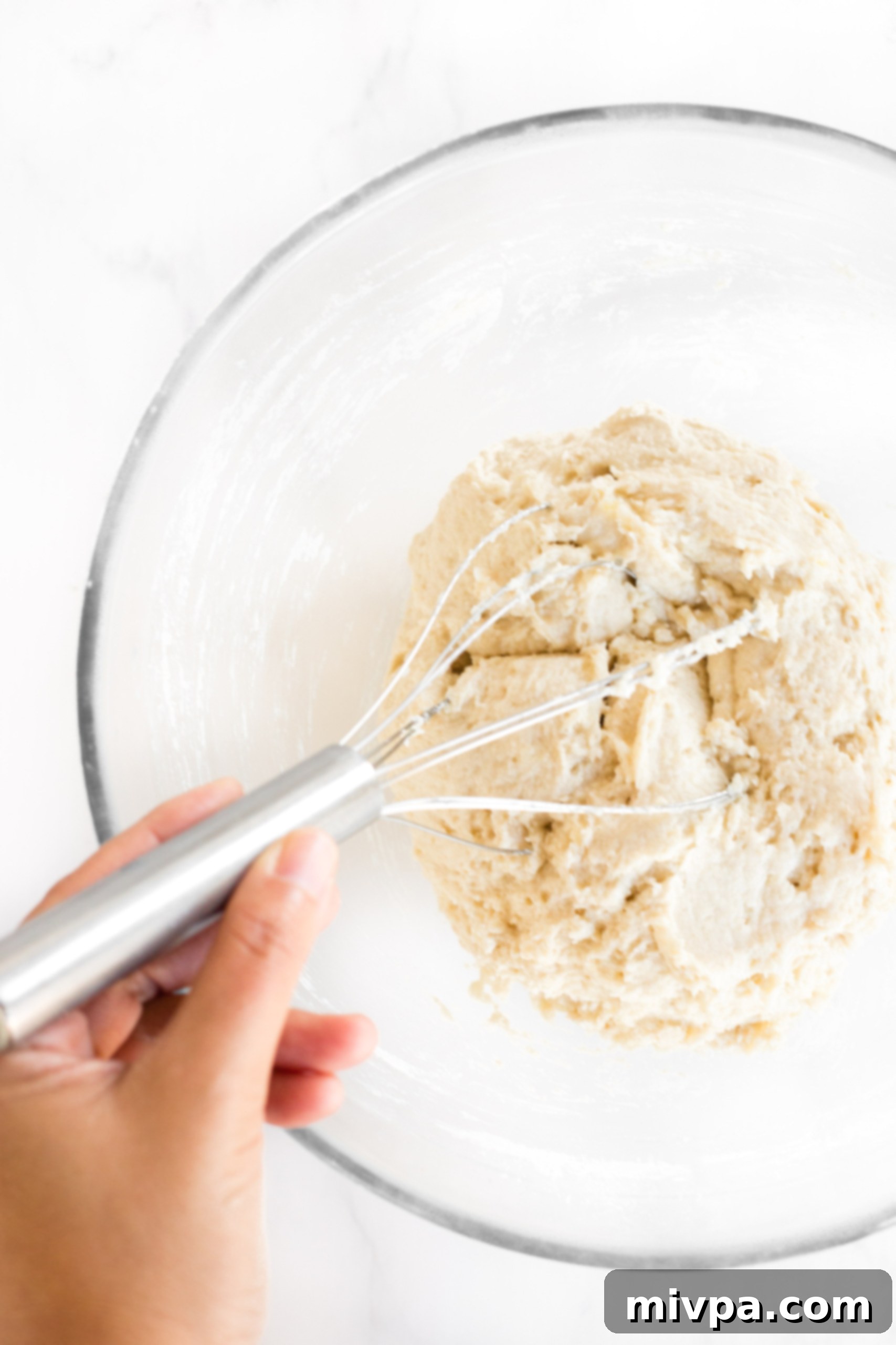 The process of mixing dough in a glass bowl, showcasing its sticky, shaggy texture.