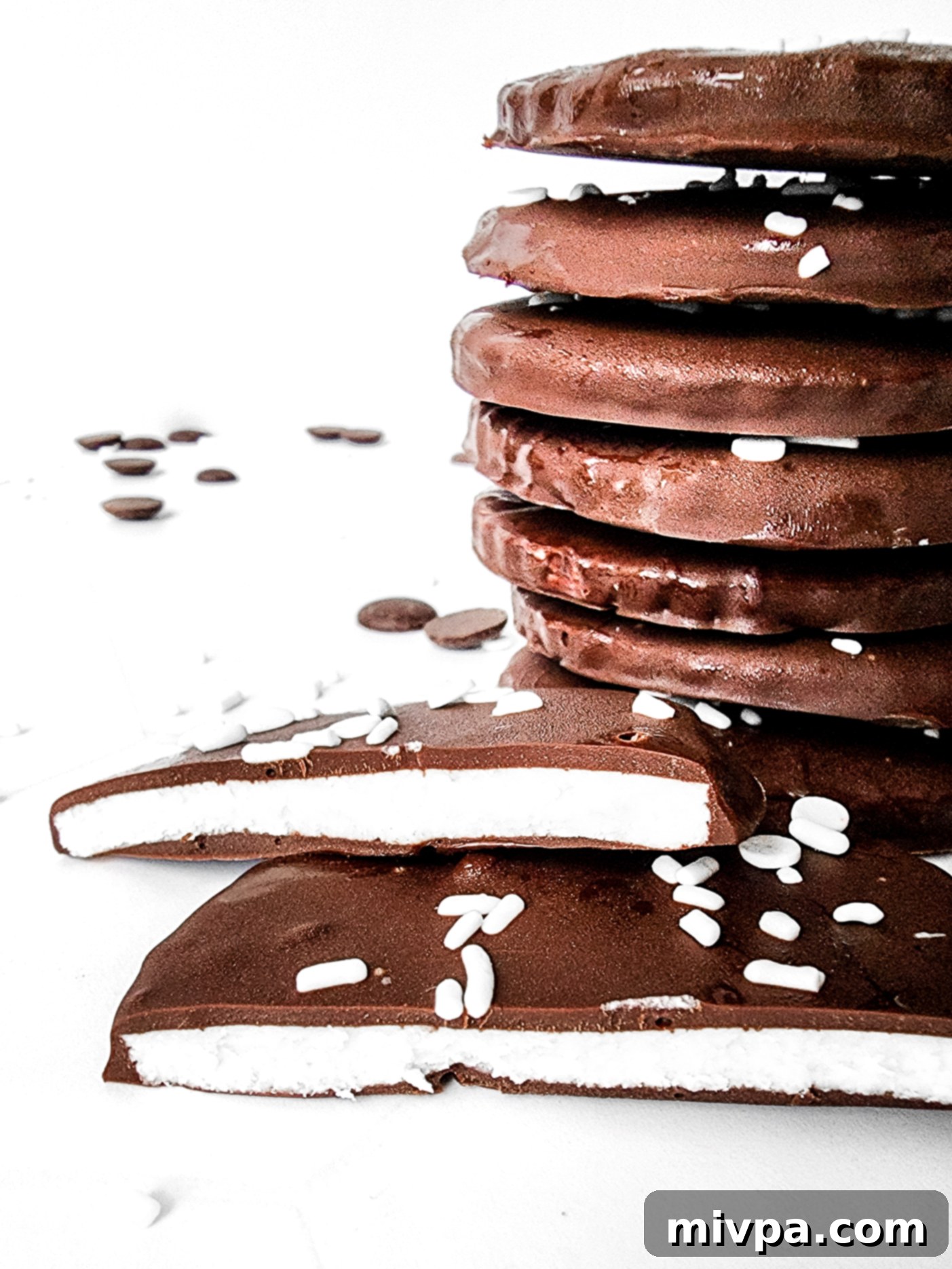 A stack of homemade peppermint patties on a white background, showcasing their dark chocolate coating and white interior.
