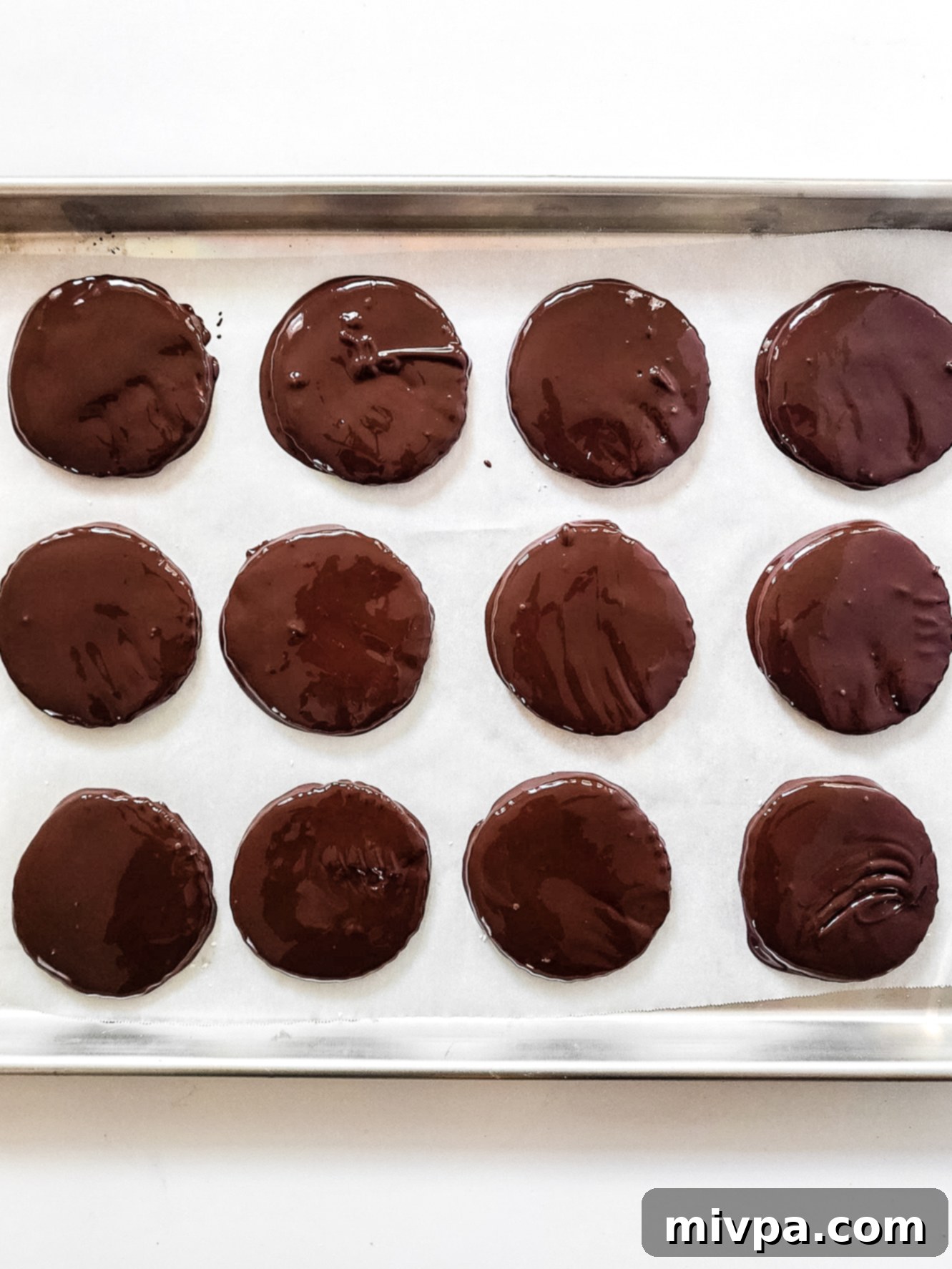 Chocolate-dipped peppermint patties setting on parchment paper on a baking sheet.