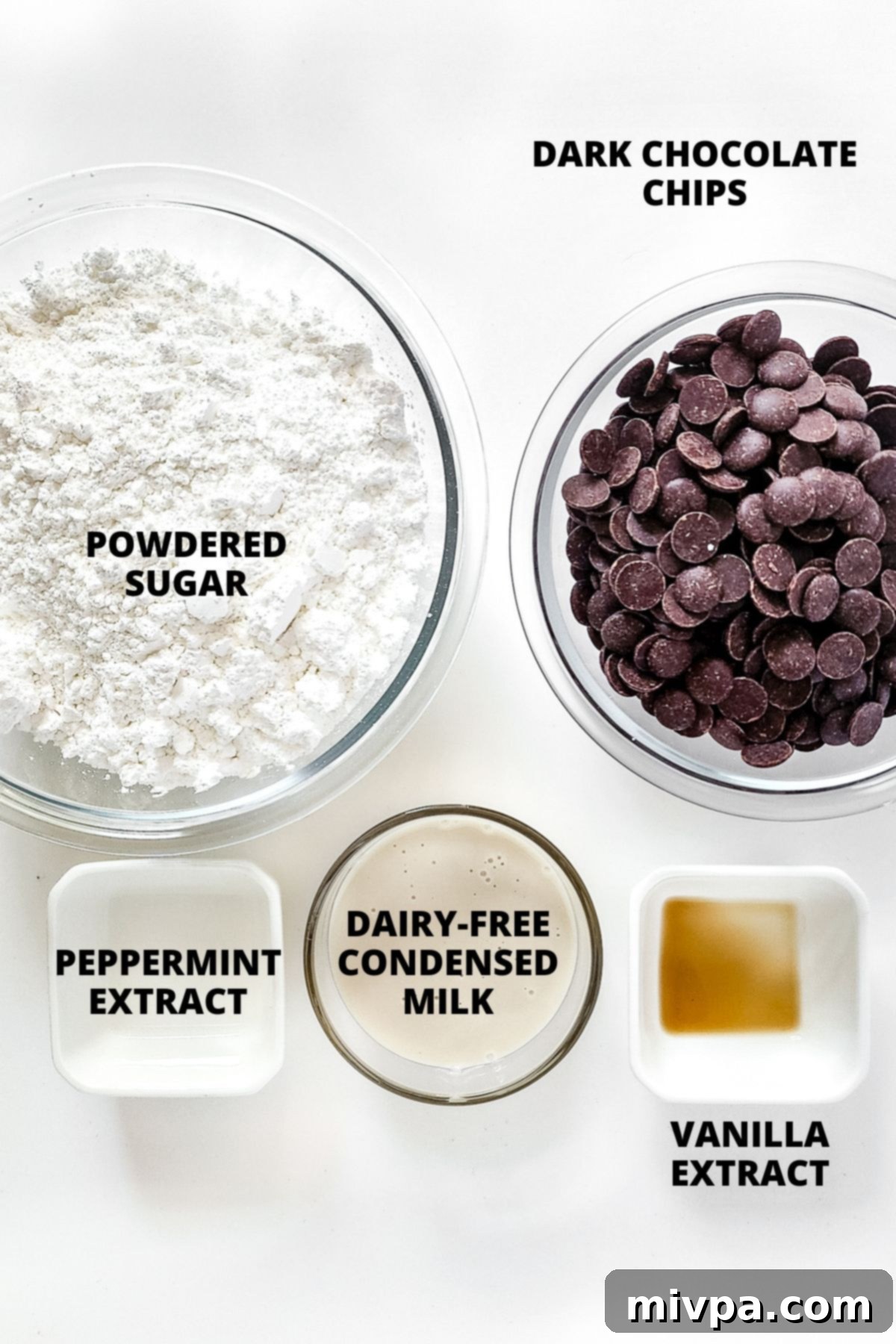 Ingredients for making gluten-free peppermint patties laid out on a marble board, including powdered sugar, condensed milk, extracts, and chocolate chips.
