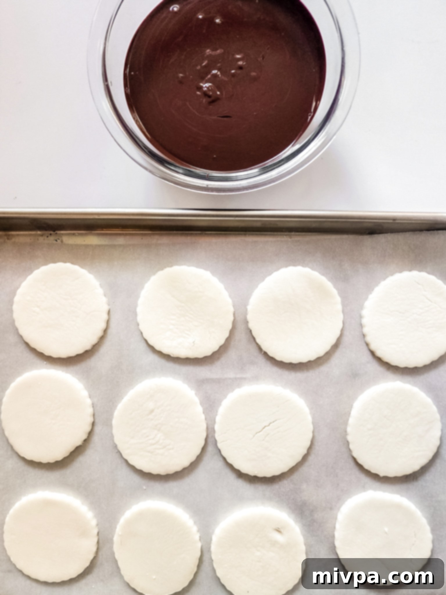 Peppermint patty circles on a parchment-lined baking sheet, next to a bowl of melted dark chocolate.