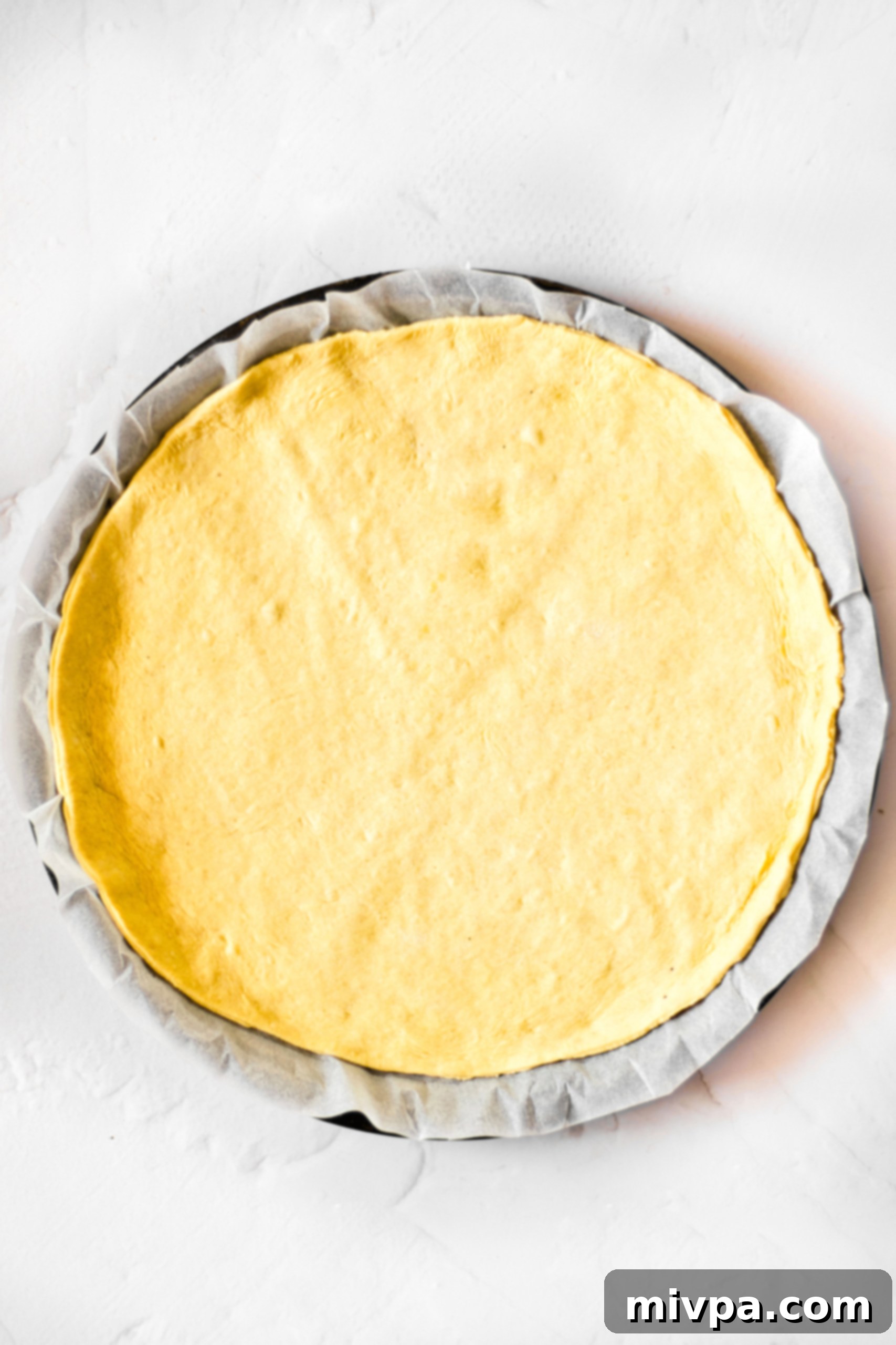 Rolled pizza dough on parchment-lined pizza baking pan.