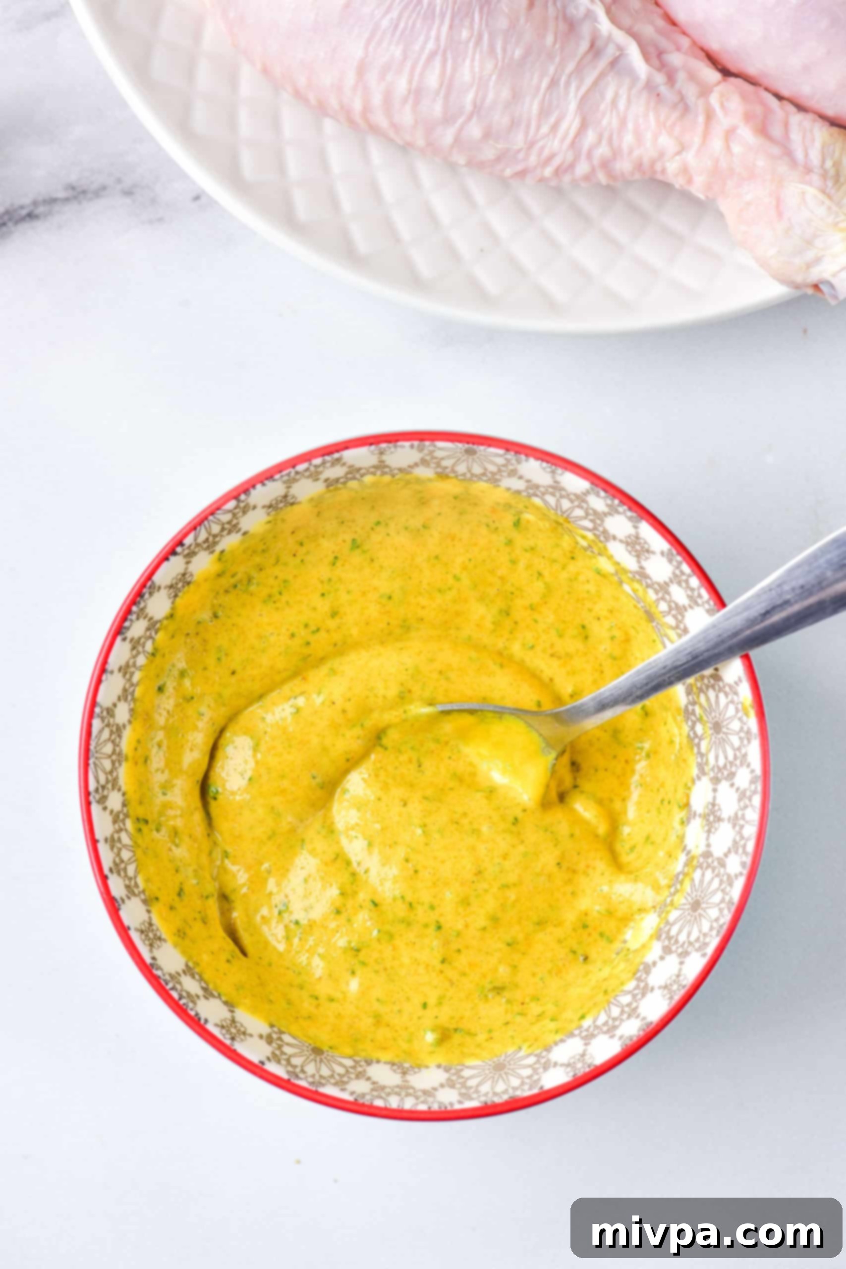 Air Fryer Chicken Quarters (Gluten-Free, Dairy-Free) A spoon in a bowl of yellow marinade.
