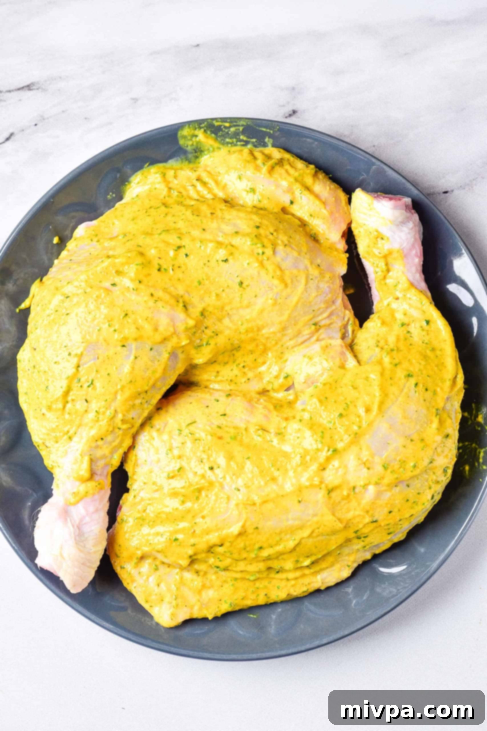 Air Fryer Chicken Quarters (Gluten-Free, Dairy-Free) Chicken leg quarters coated with yellow marinade in a grey bowl.