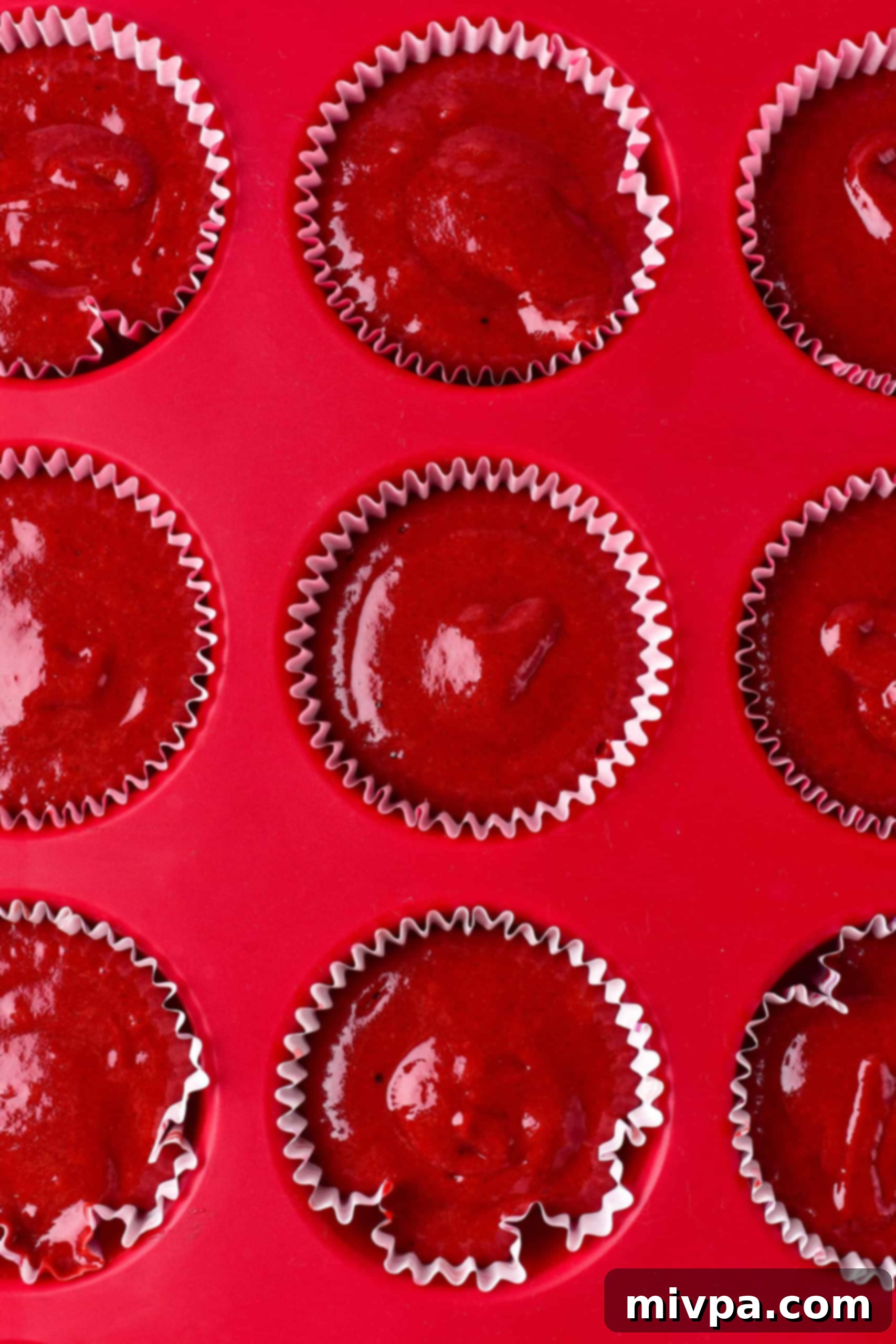 Red velvet cupcake batter in lined muffin tin.