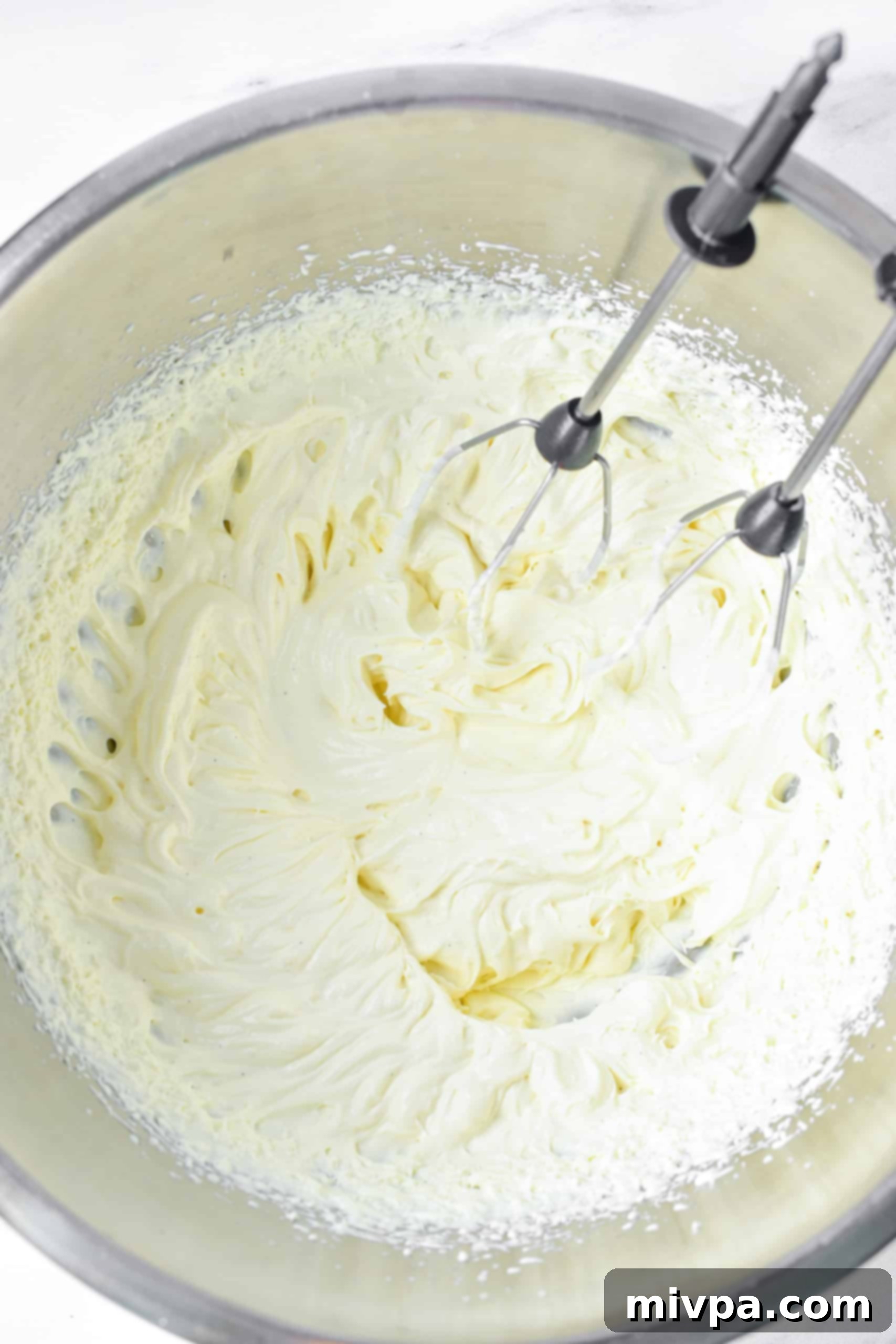 Whipping cream with stiff peaks in metal bowl.