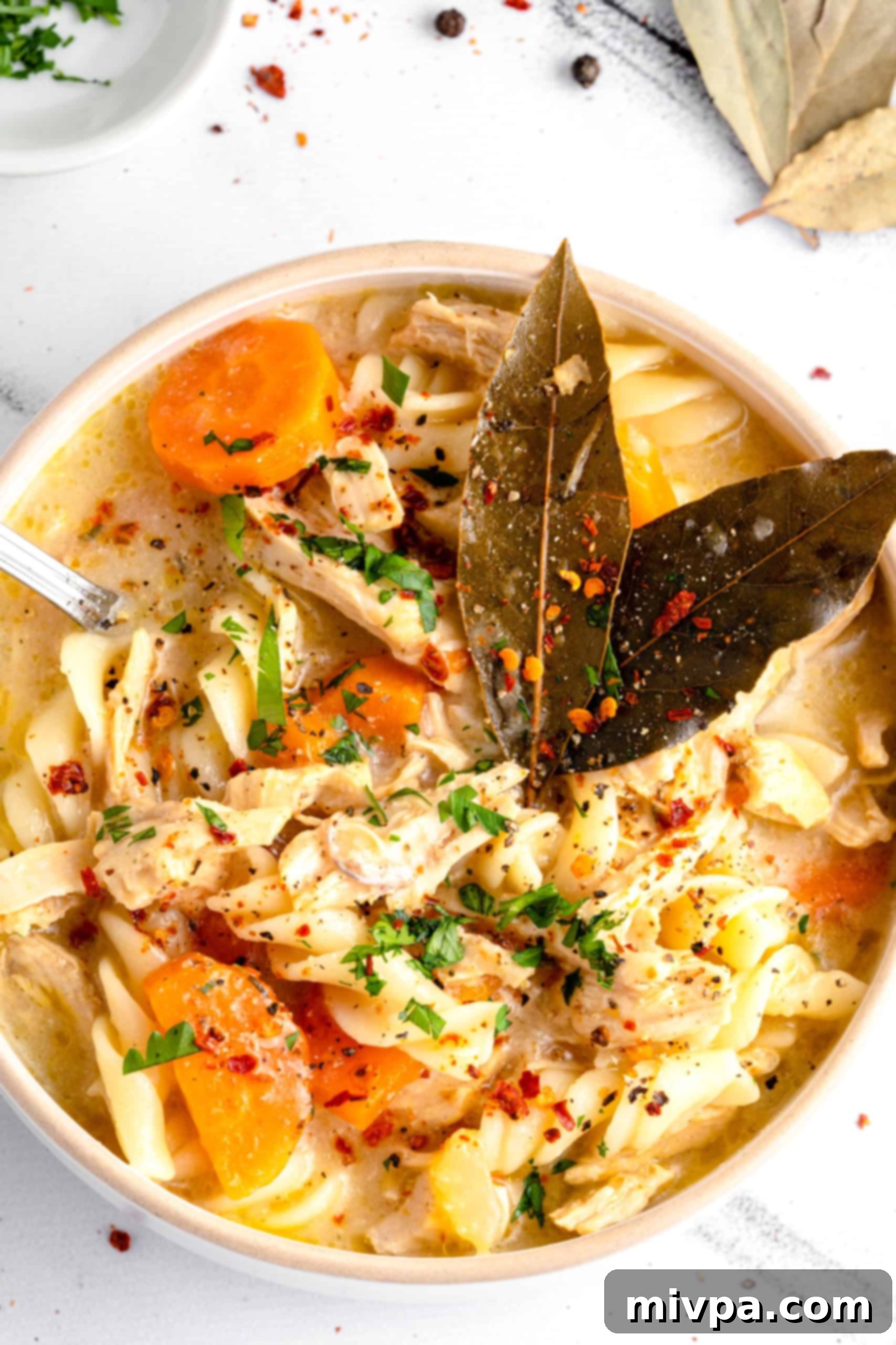 Gluten-Free Chicken Noodle Soup (Dairy-Free) for Cold Weather A comforting bowl of homemade gluten-free chicken noodle soup, garnished with bay leaves and fresh parsley, ready to be enjoyed on a cold day.