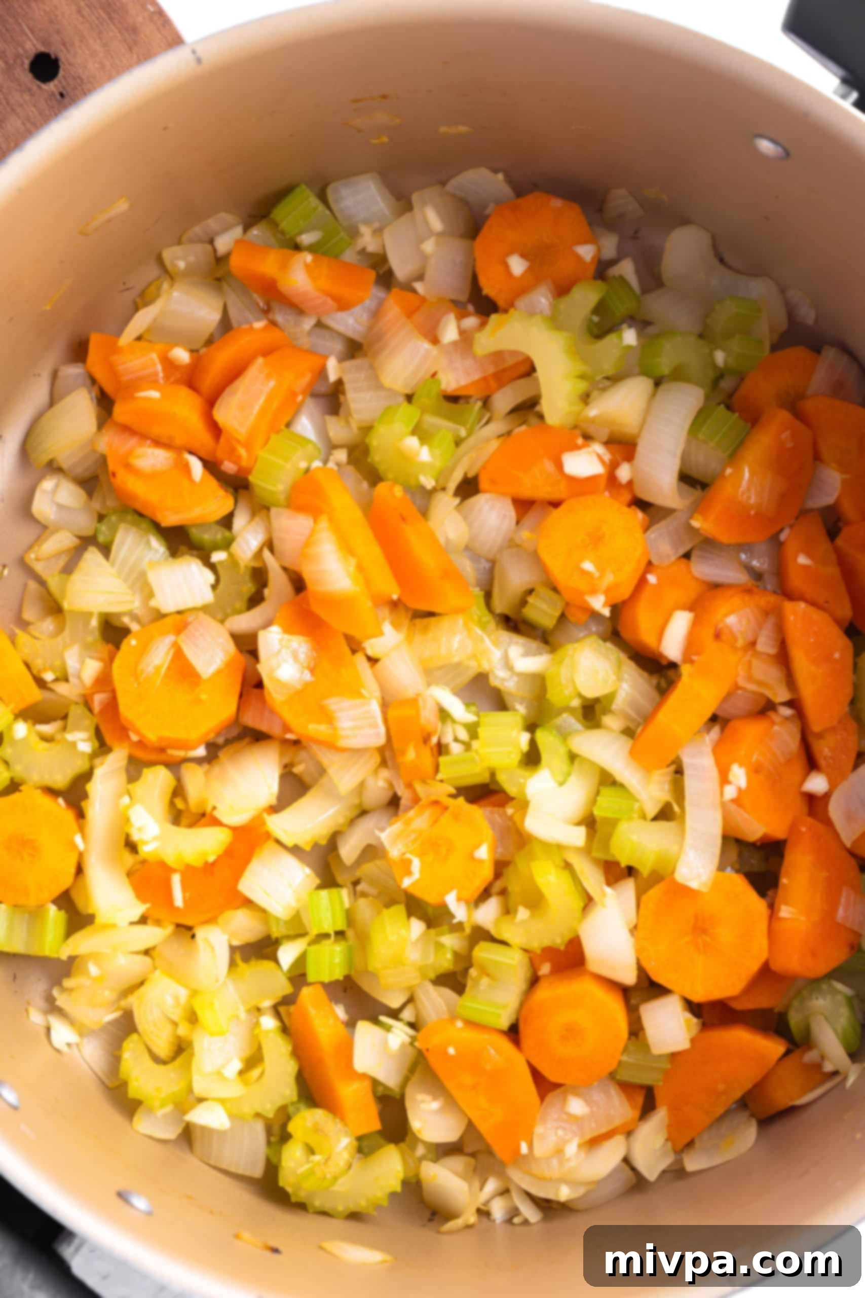 Sautéing Vegetables for Gluten-Free Chicken Soup (Dairy-Free) Chopped carrots, onions, and celery sautéing in olive oil in a large pot, forming the aromatic base for the chicken noodle soup.